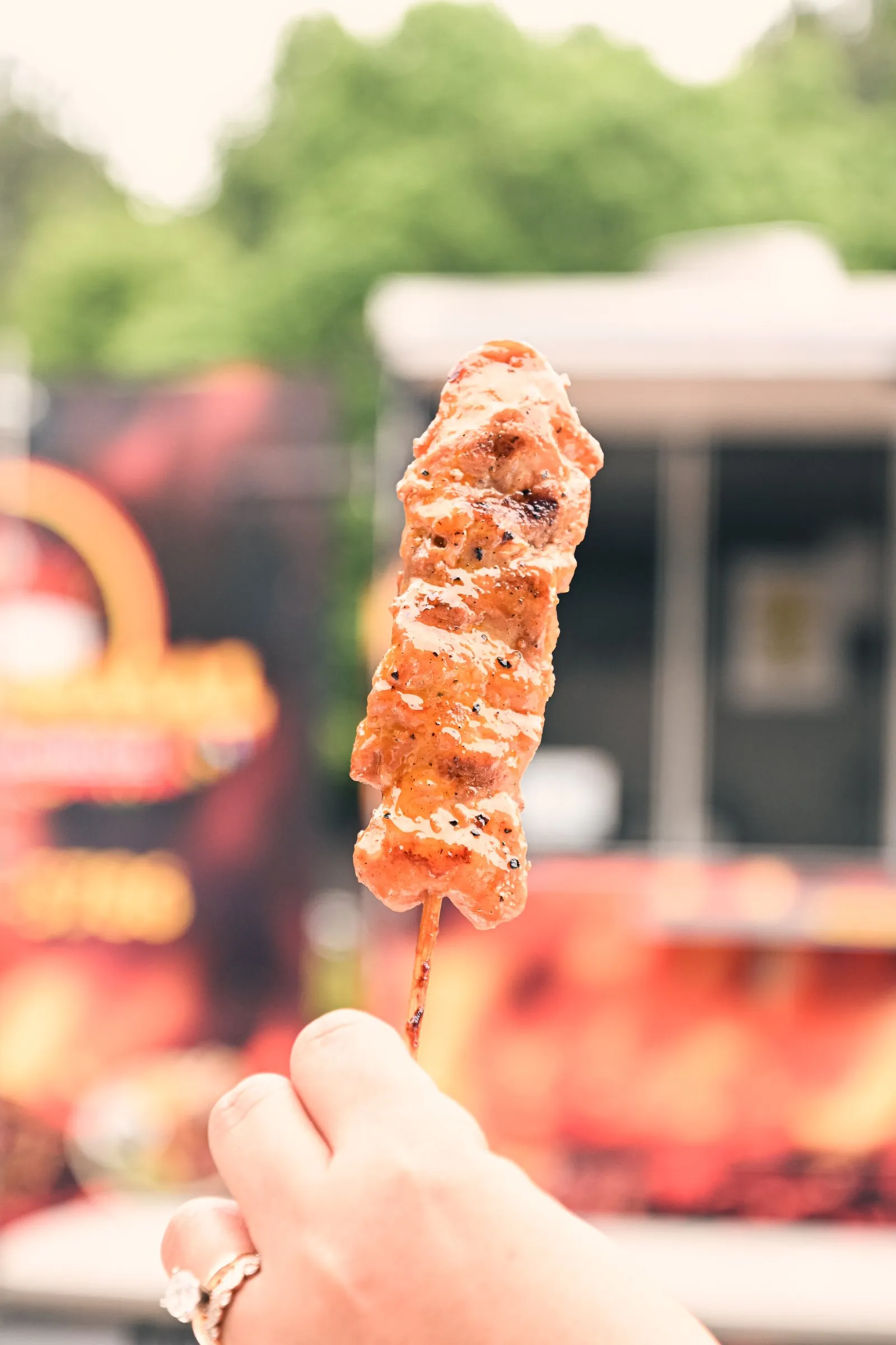A glazed barbecue skewer held up against the flame-painted food truck