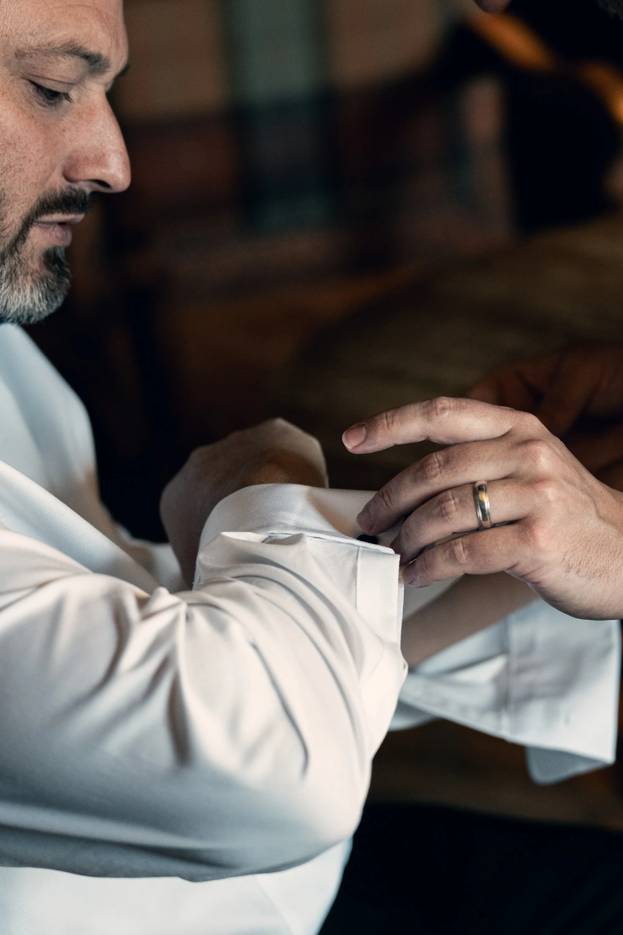 Groom in a white shirt fastening his cuff, wedding band on his finger, Cinema Slate edit