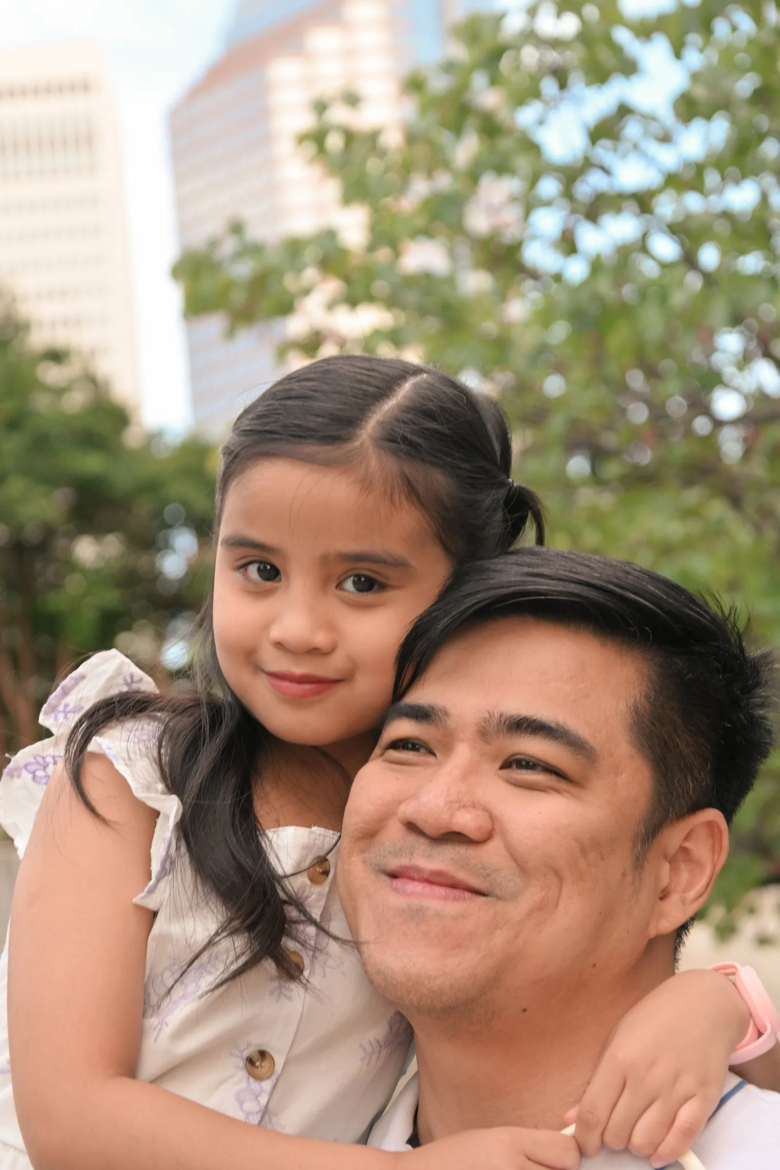 Their daughter hugging Jet from behind, cheek to cheek, with Uptown towers behind them
