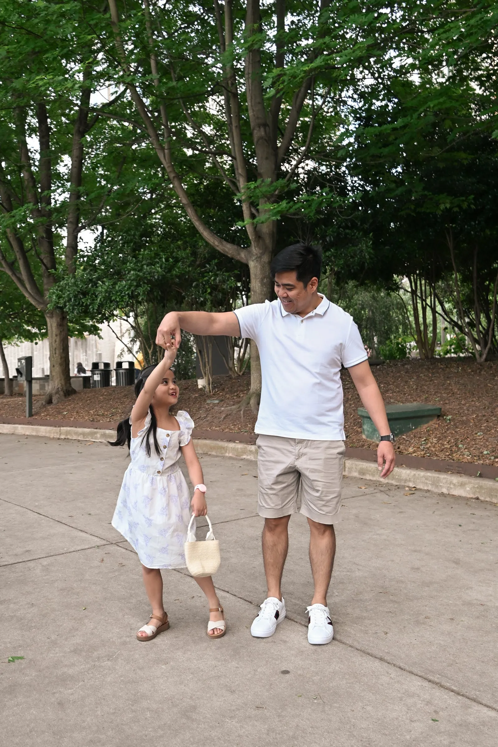 Jet twirls his daughter on the park path under the trees