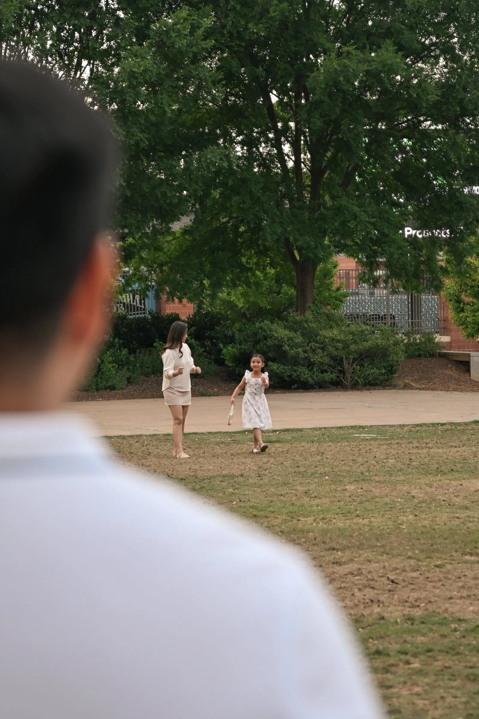Over Jet's shoulder as Jessica and their daughter play on the lawn
