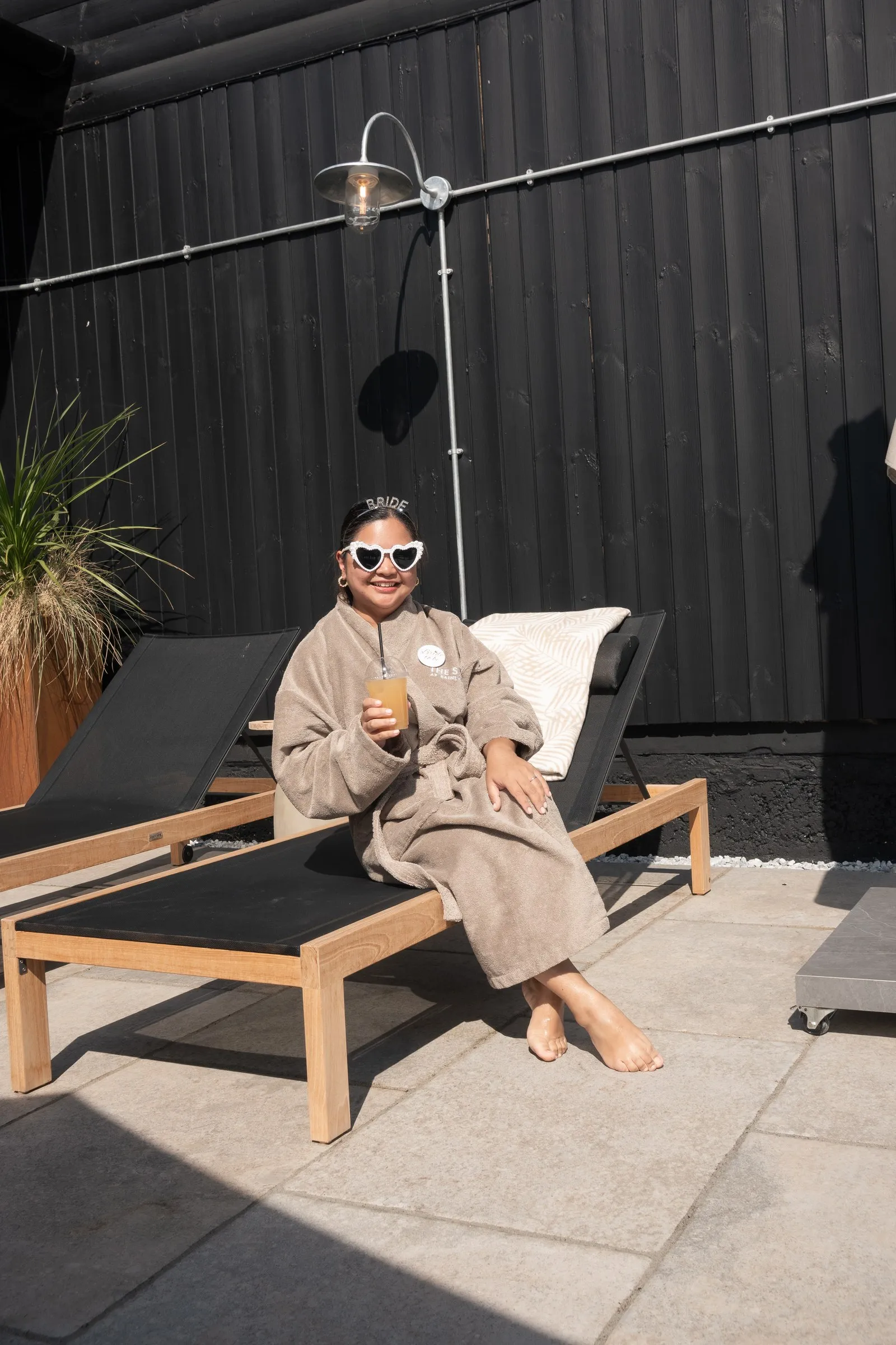 A guest in a robe and heart sunglasses relaxing on a sun lounger with a cocktail