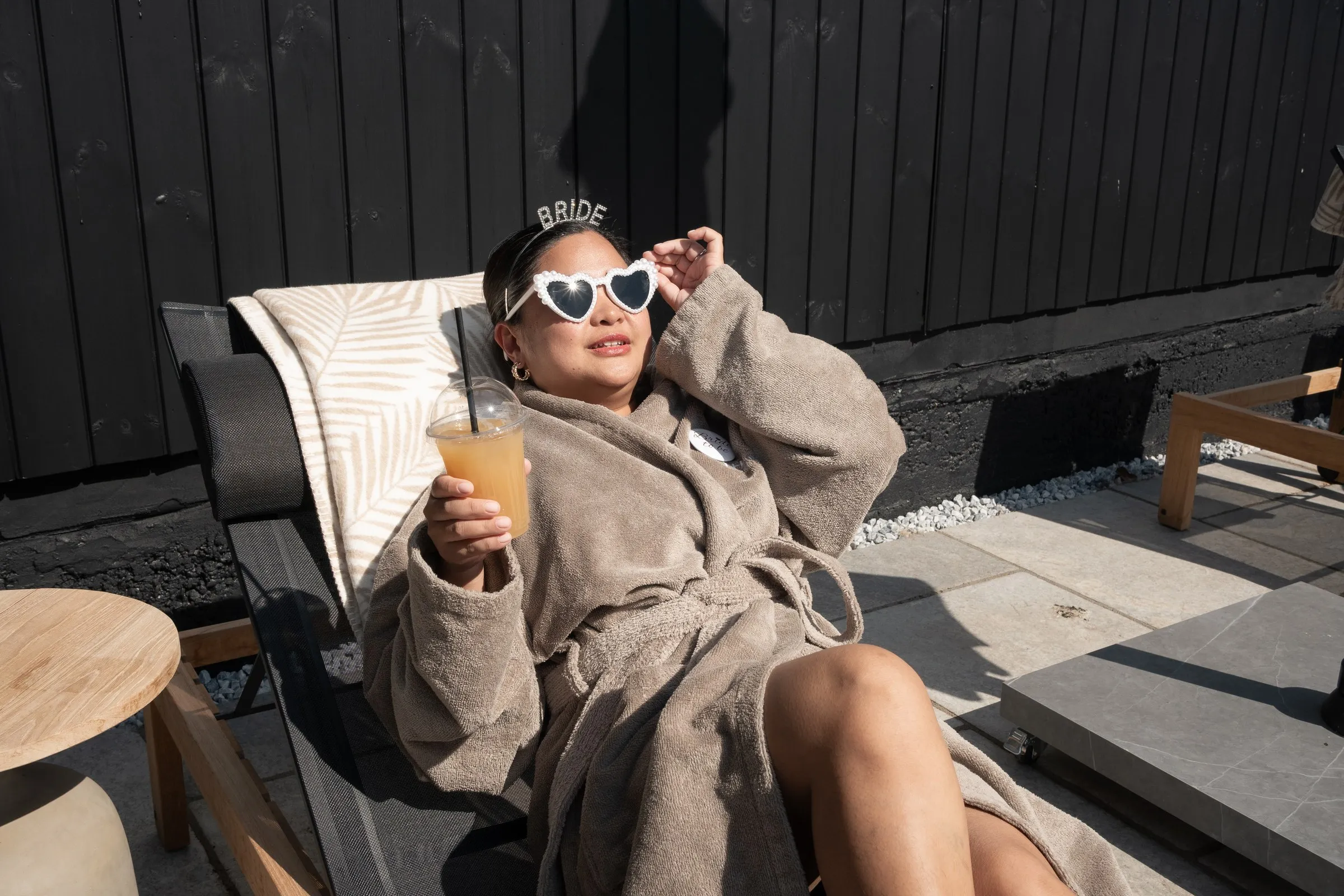 Mathelle in heart sunglasses and a Bride headband lounging with an orange cocktail
