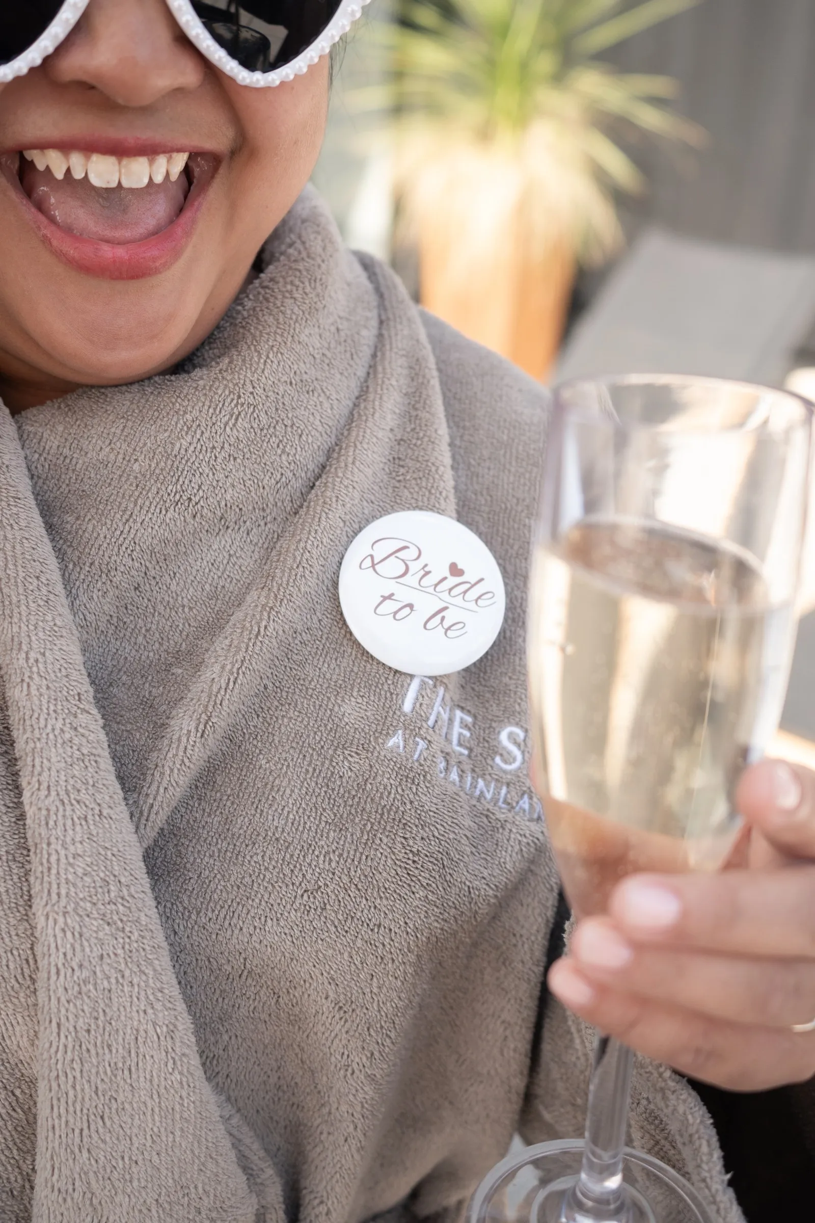 Mathelle laughing with a glass of champagne, a Bride to be pin on her robe