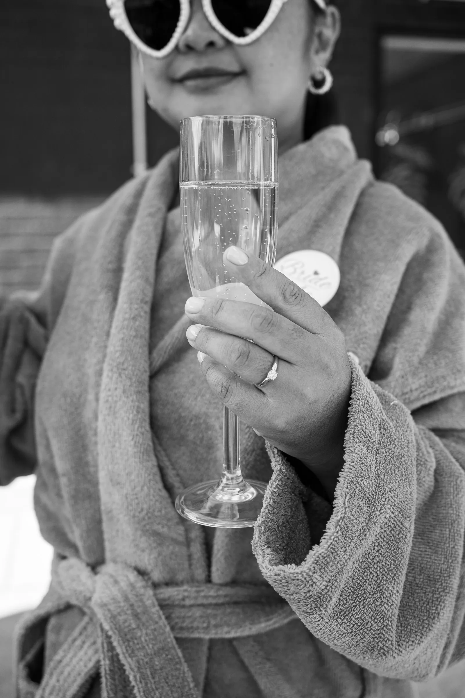 Black and white close-up of Mathelle holding a champagne flute, her engagement ring on her finger