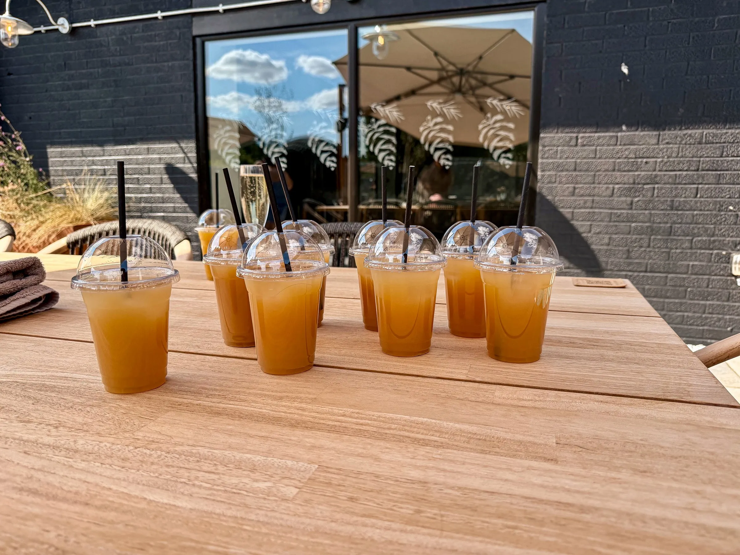 A row of orange cocktails lined up on a wooden patio table