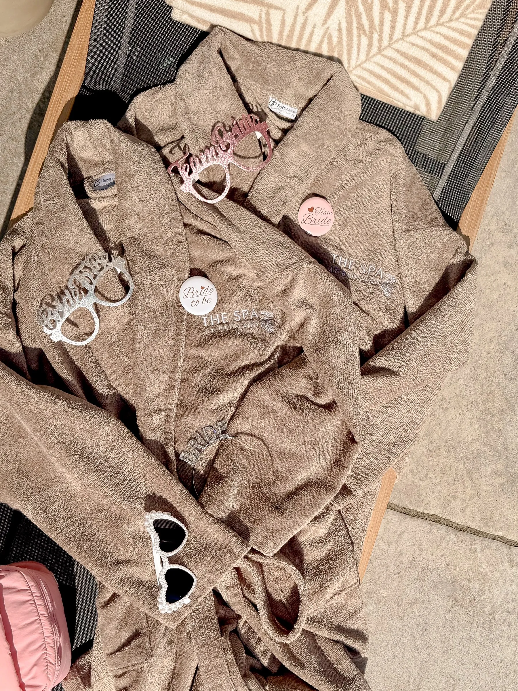 Robes with Team Bride pins and heart sunglasses laid out on a lounger