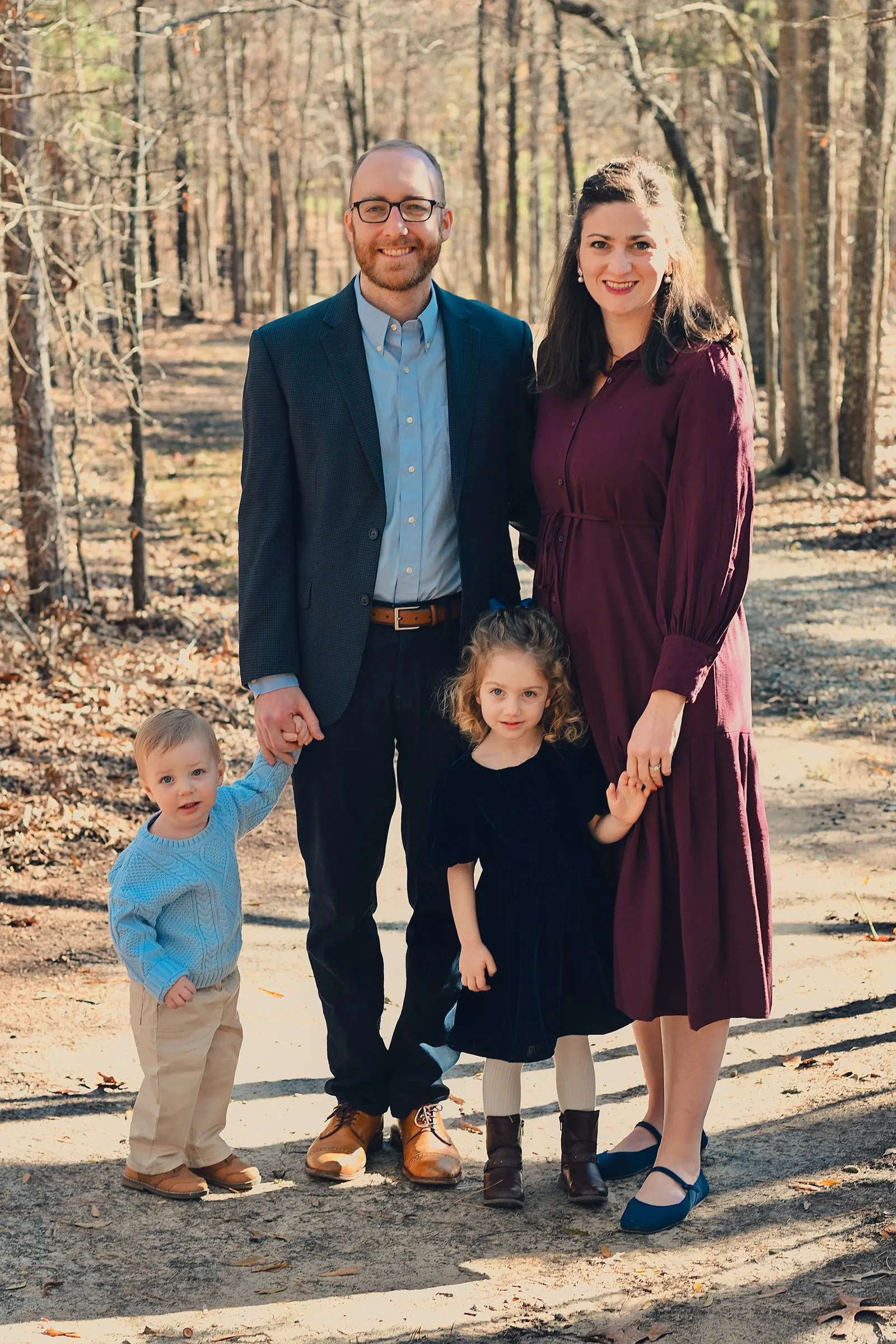 Matt, Olivia, their daughter, and their son holding hands on a wooded trail at Marvin Efird Park