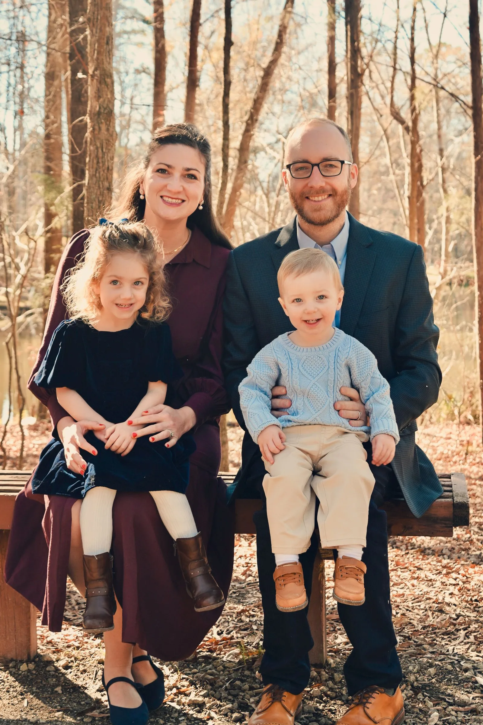 The family on a wooden bench by the pond, their daughter on Olivia's lap and their son on Matt's