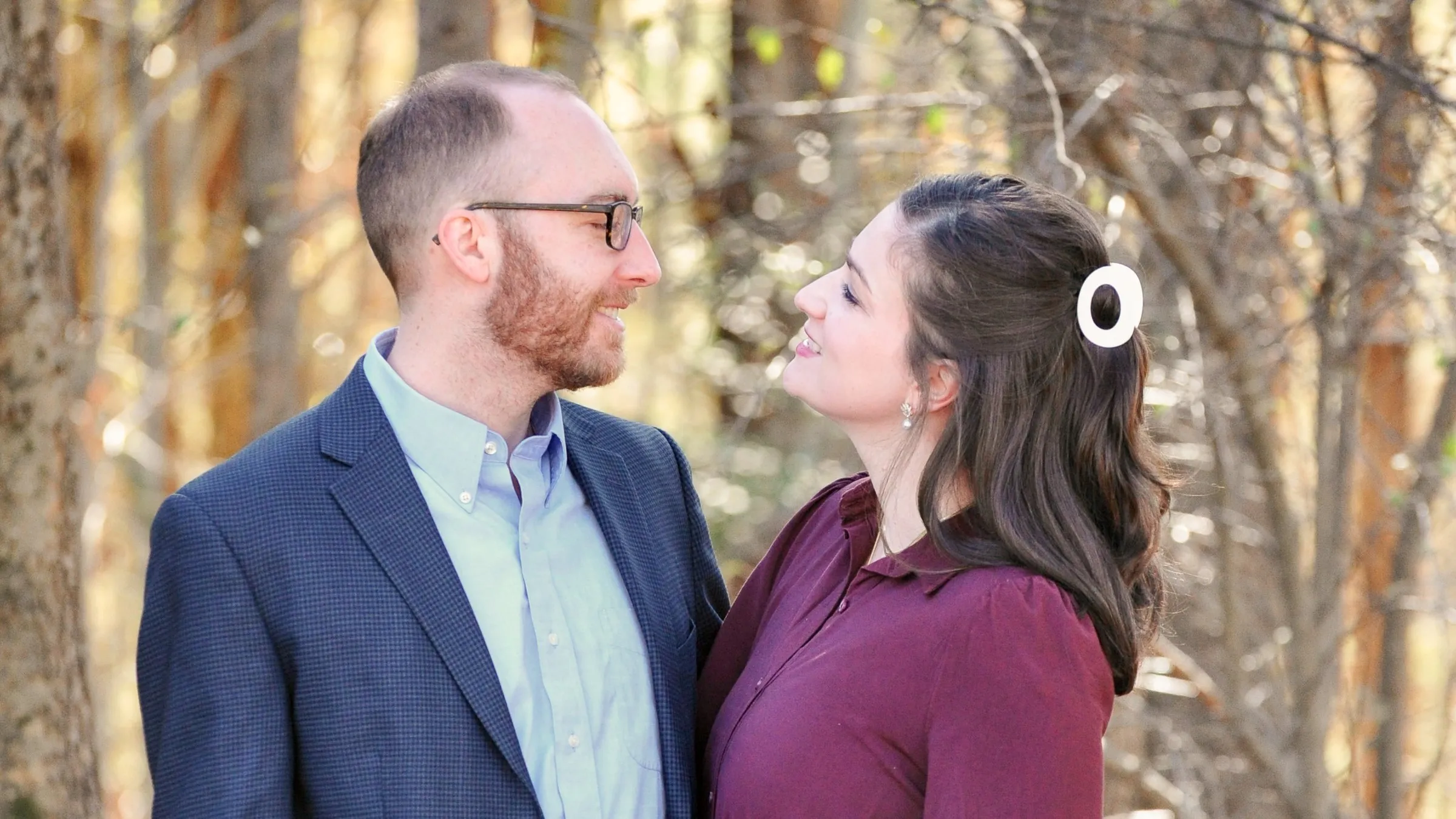Matt and Olivia looking at each other and smiling in the woods, a white clip in her hair