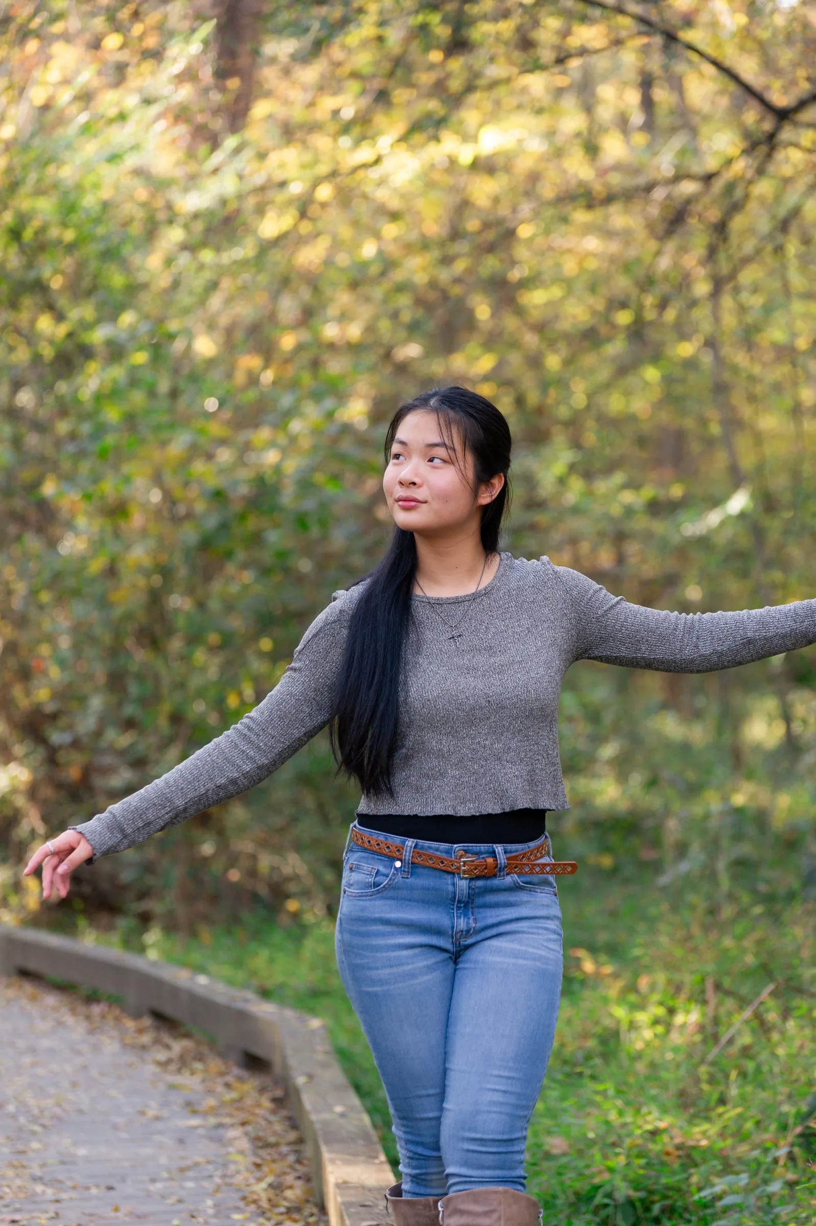 Meilin with her arms open on a wooden boardwalk, looking up into the yellow autumn leaves