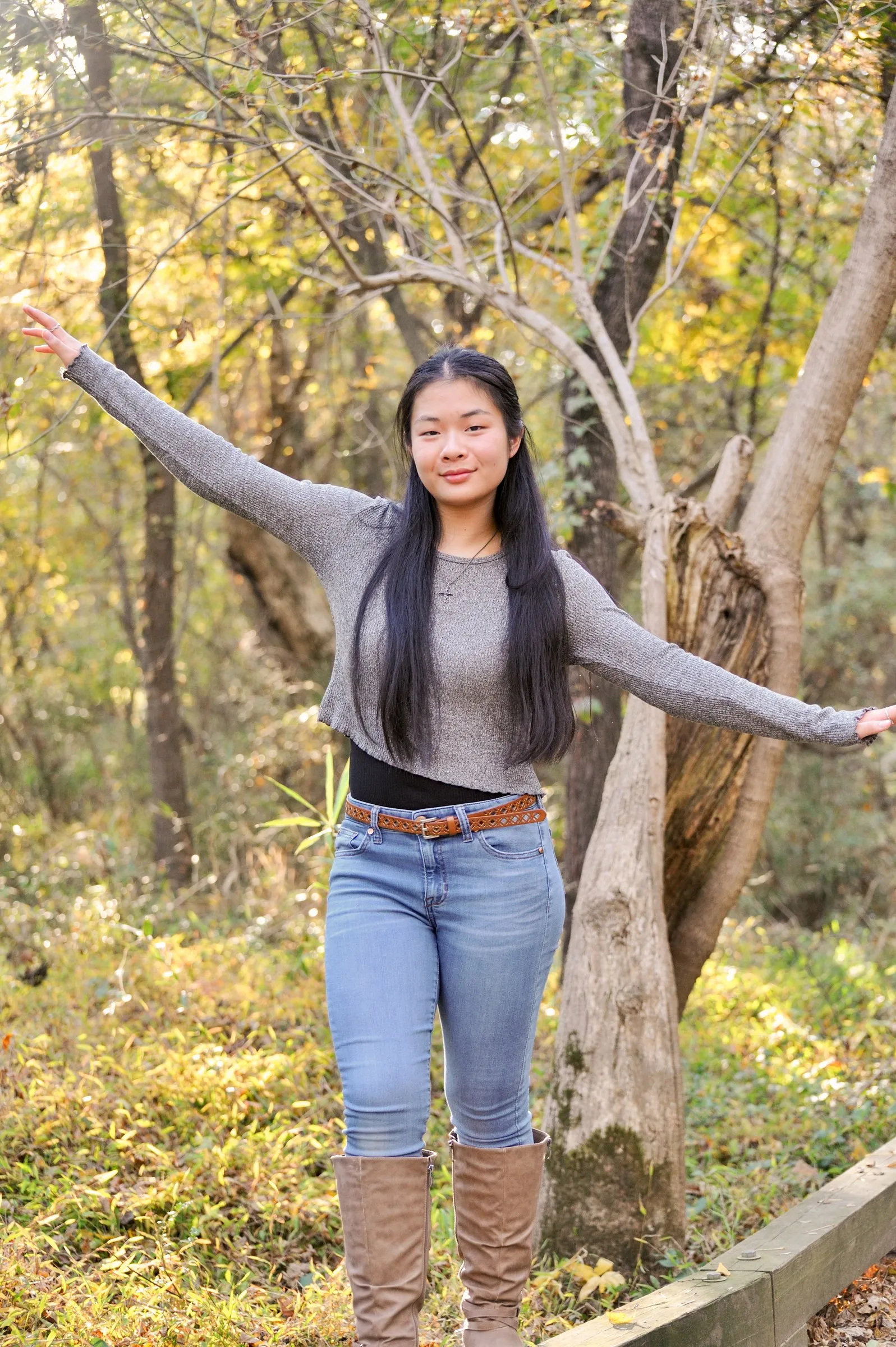 Meilin smiling with her arms spread wide among golden trees beside the trail