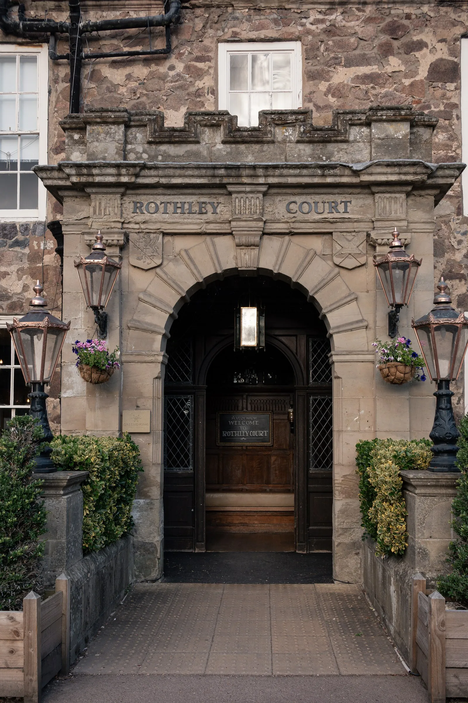The arched stone entrance of Rothley Court framed by lanterns and flower boxes