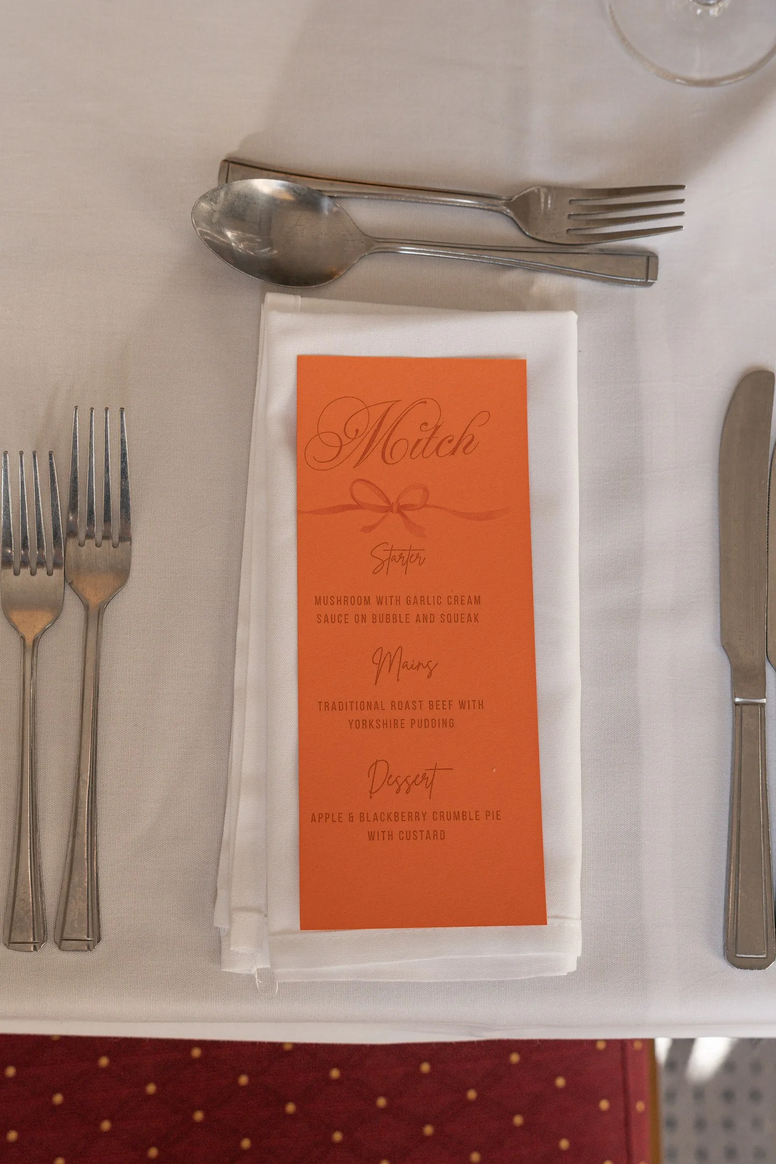 Peach menu card with Mathelle's name in script on a white napkin beside polished silverware