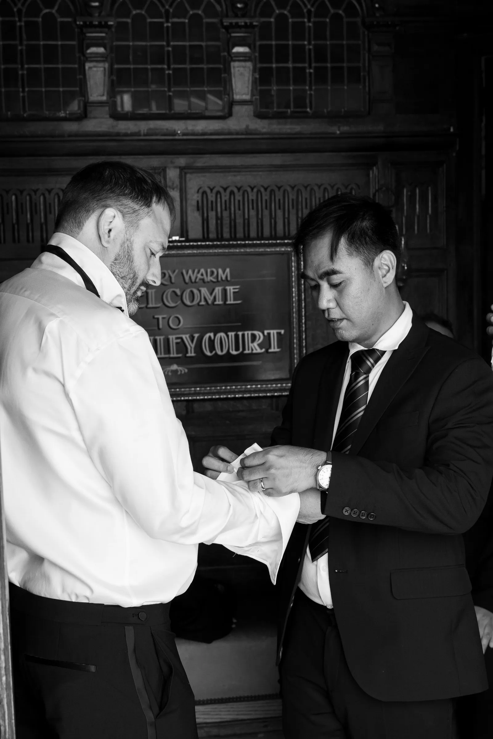 Black and white frame of Mitch getting help with his cufflinks