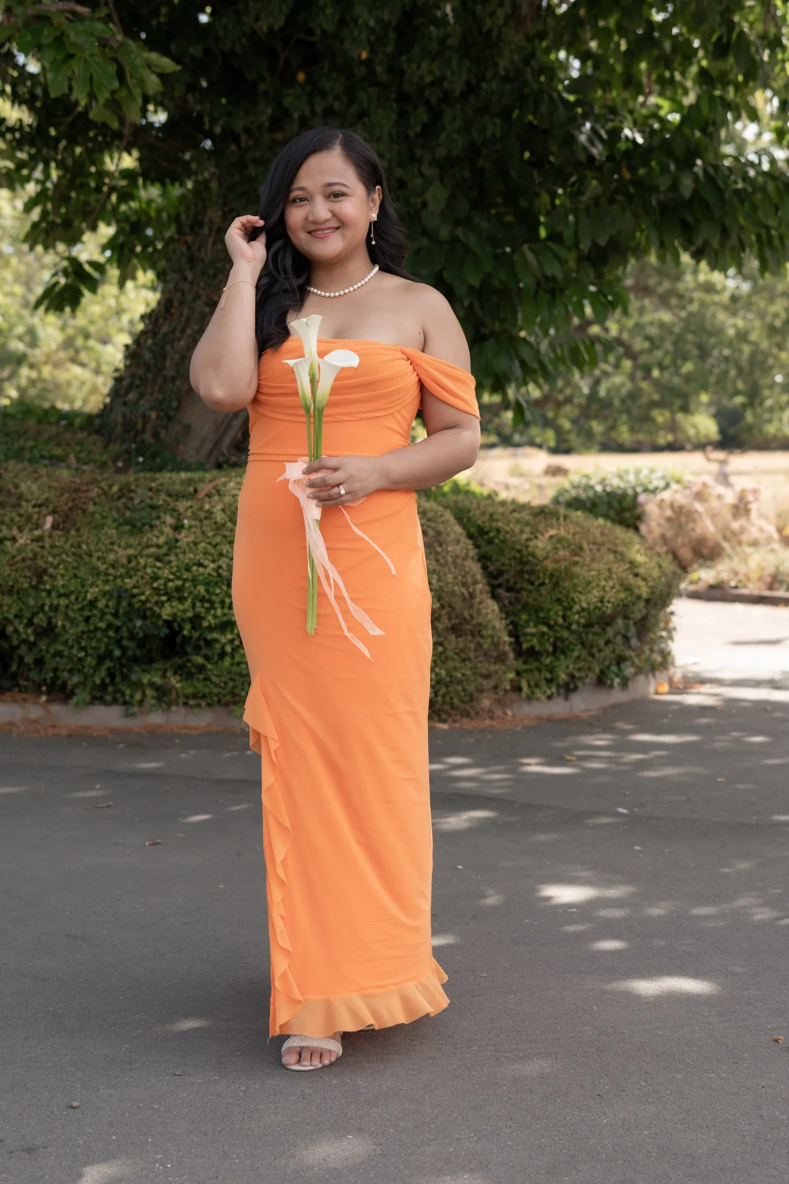 Bridesmaid in peach holding calla lilies beneath a shade tree