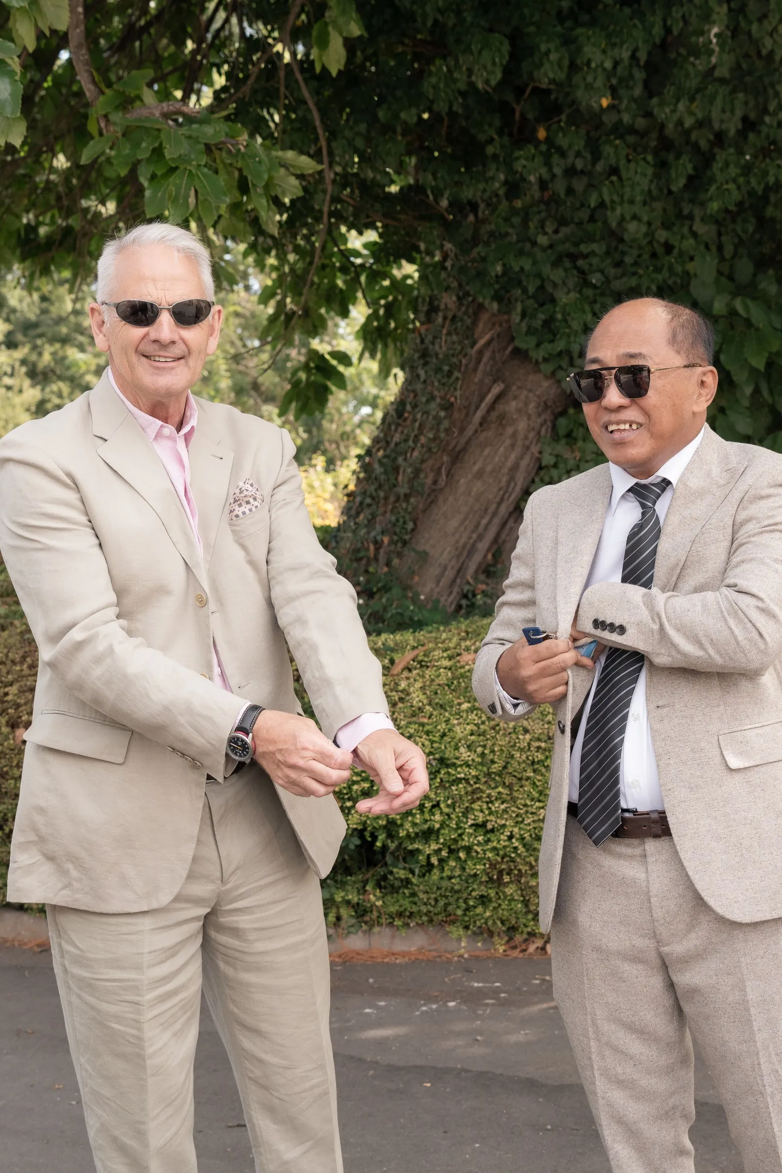 Two guests in cream suits and sunglasses laughing in the garden