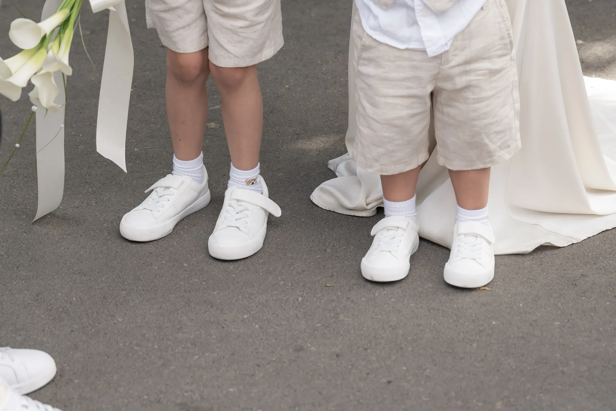 Close-up of small white shoes beside the hem of Mathelle's gown