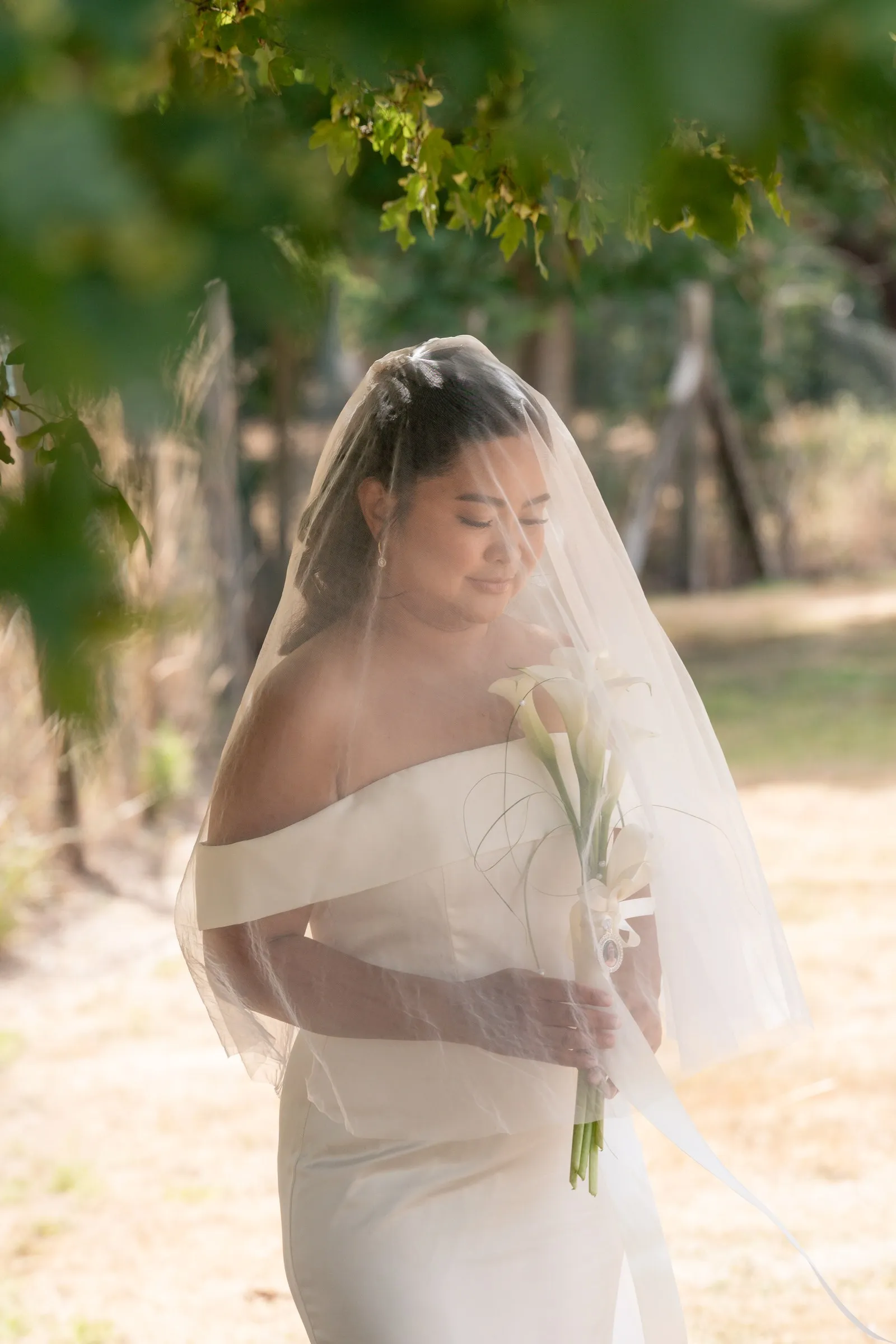 Mathelle under her veil holding calla lilies in dappled light