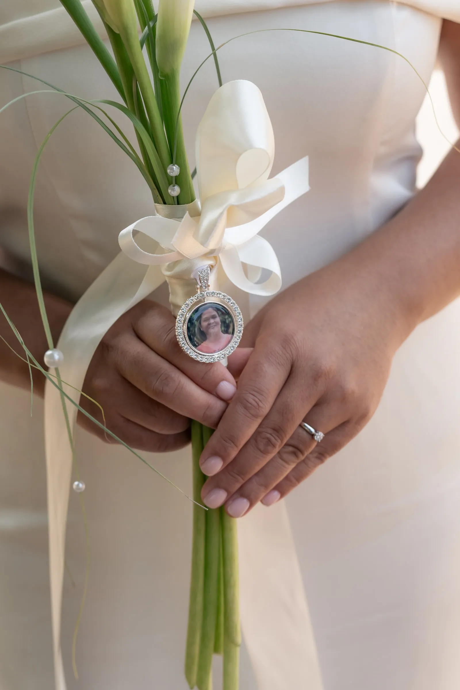 Close-up of Mathelle's calla lily bouquet with a keepsake locket charm and her wedding ring at Rothley Court