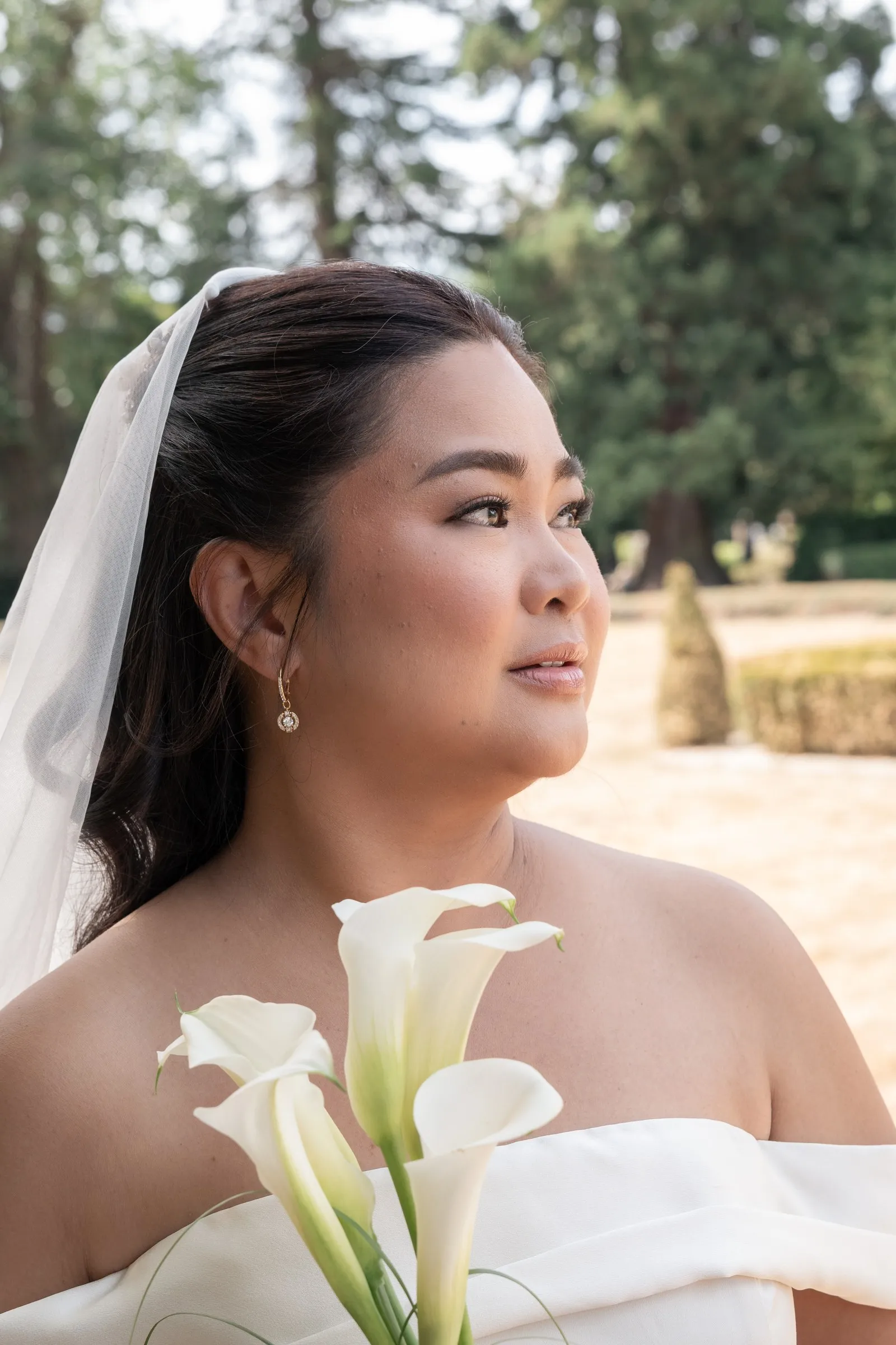 Bridal portrait of Mathelle holding calla lilies against the trees at Rothley Court