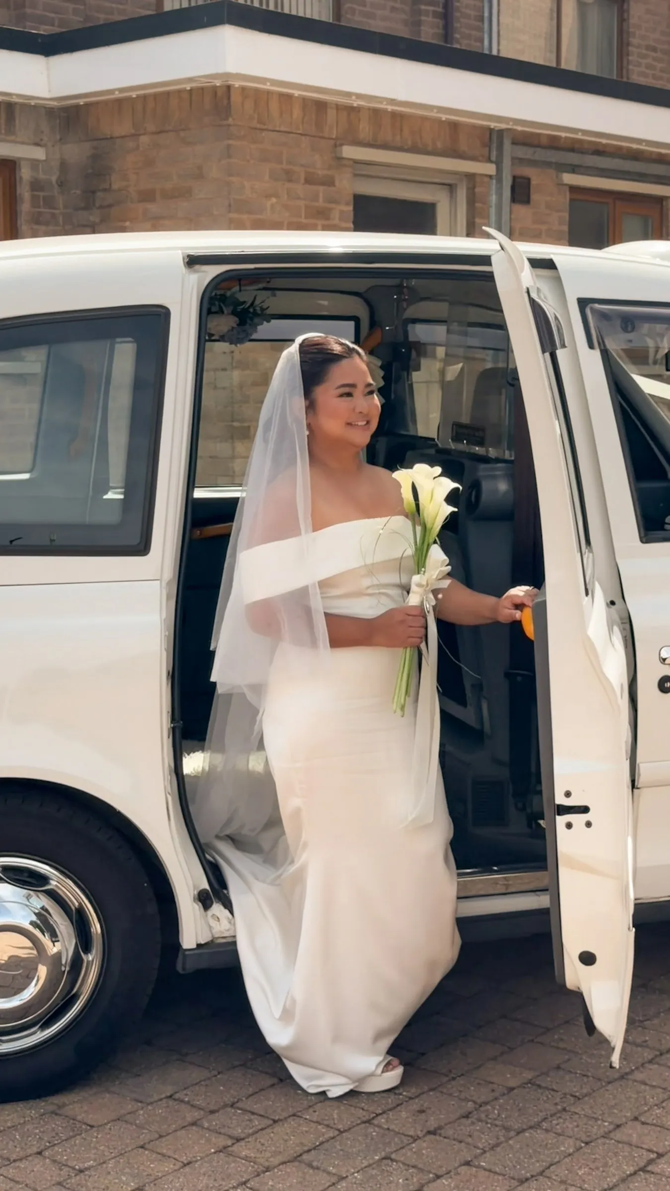 Mathelle stepping out of a white London taxi with her calla lily bouquet as she arrives at Rothley Court