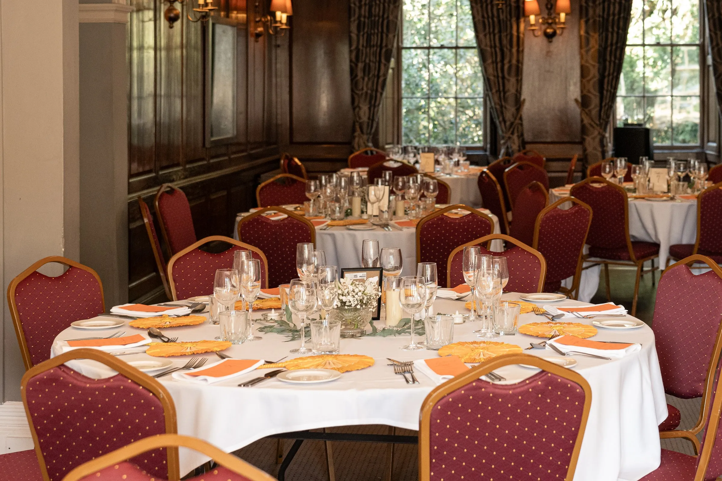 Rothley Court's wood paneled reception room set with round tables, peach fans and red chairs