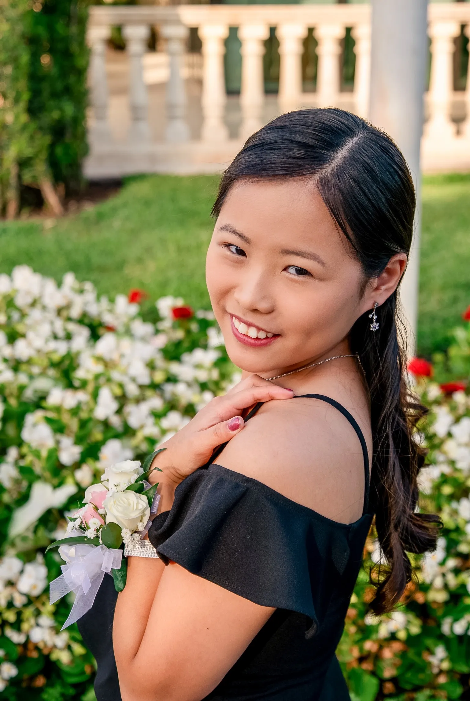 Mya smiling with her hand on her shoulder and a rose corsage on her wrist, white flowers behind her