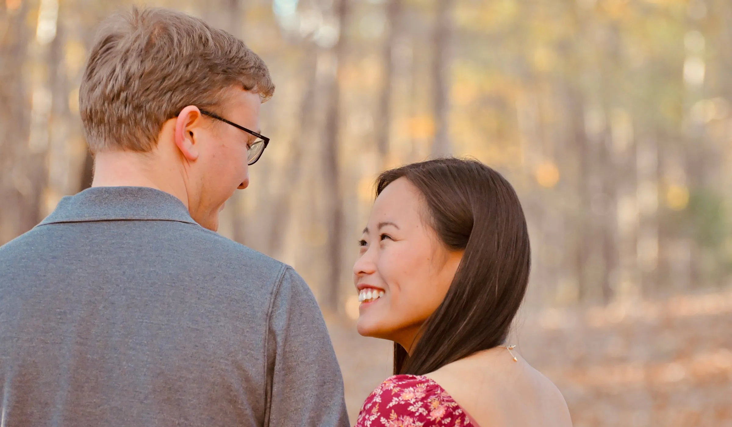 Over Jacob's shoulder, Mya smiling up at him with the fall woods soft behind her