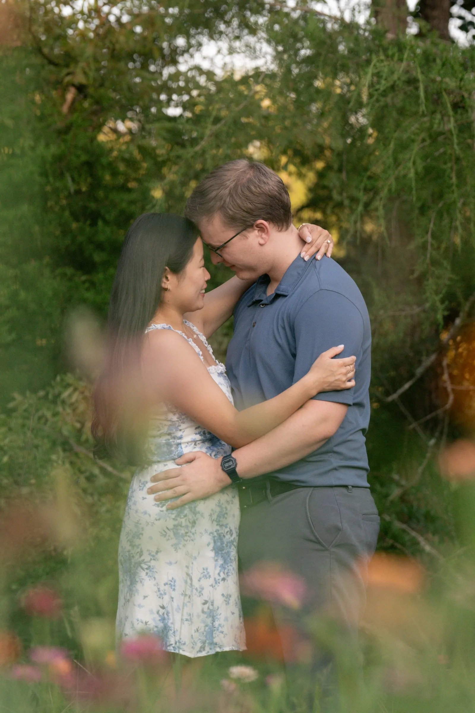 Jacob holding Mya close among the wildflowers, blooms soft in the foreground