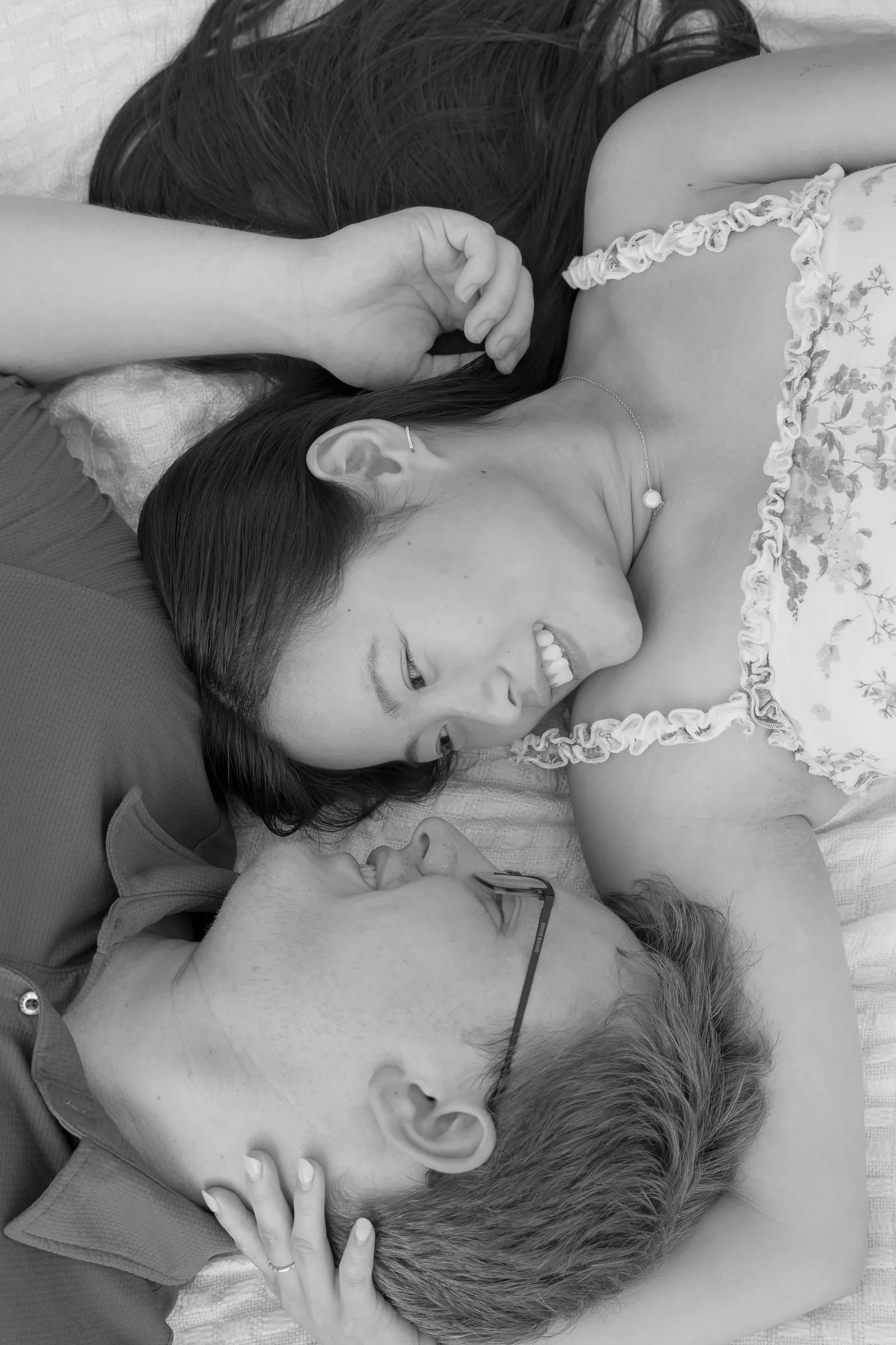 Black and white photograph of Mya and Jacob lying head to head on a blanket, smiling, at Marvin Efird Park in Waxhaw, NC