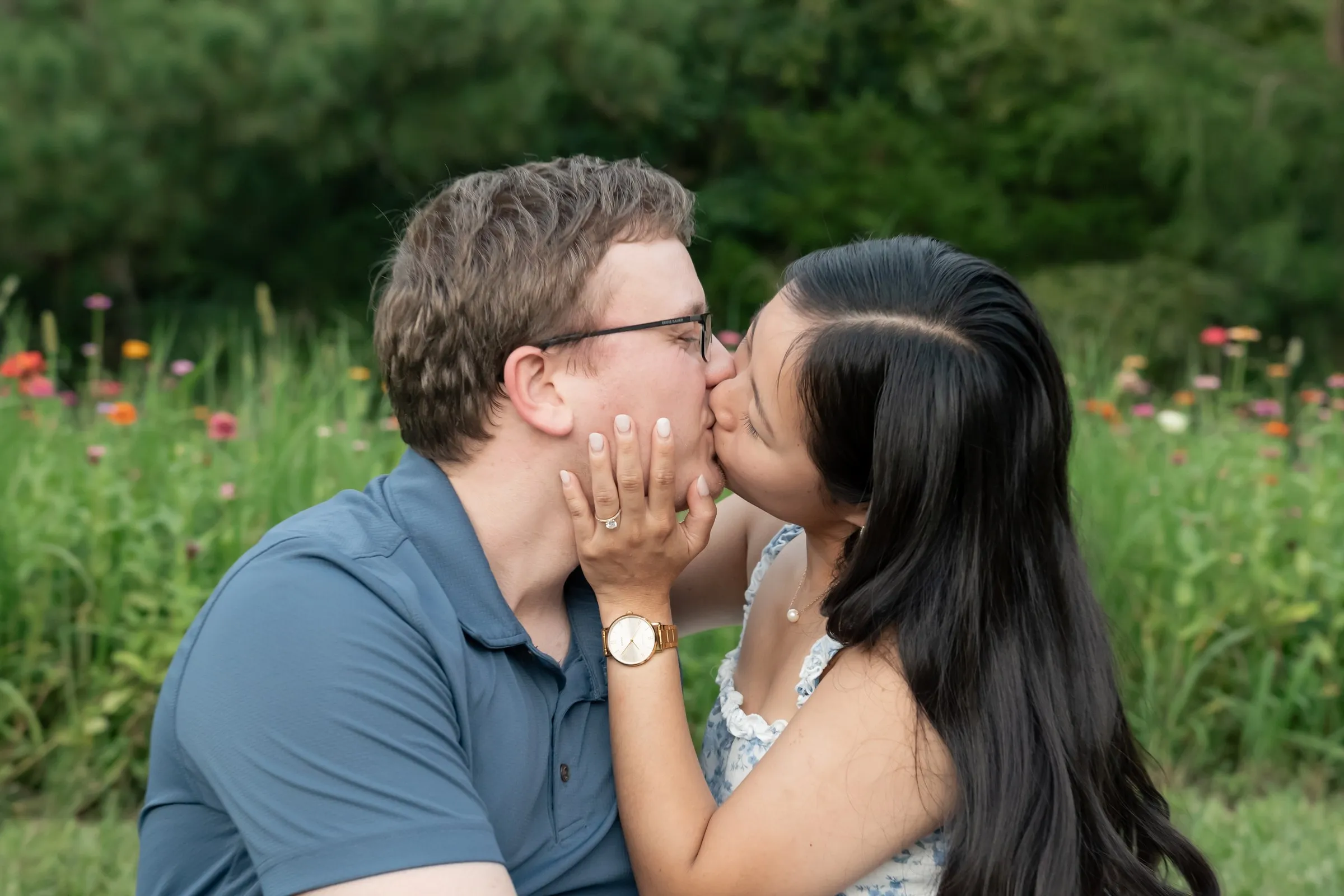 Mya kissing Jacob with her hand on his cheek, seated in the grass
