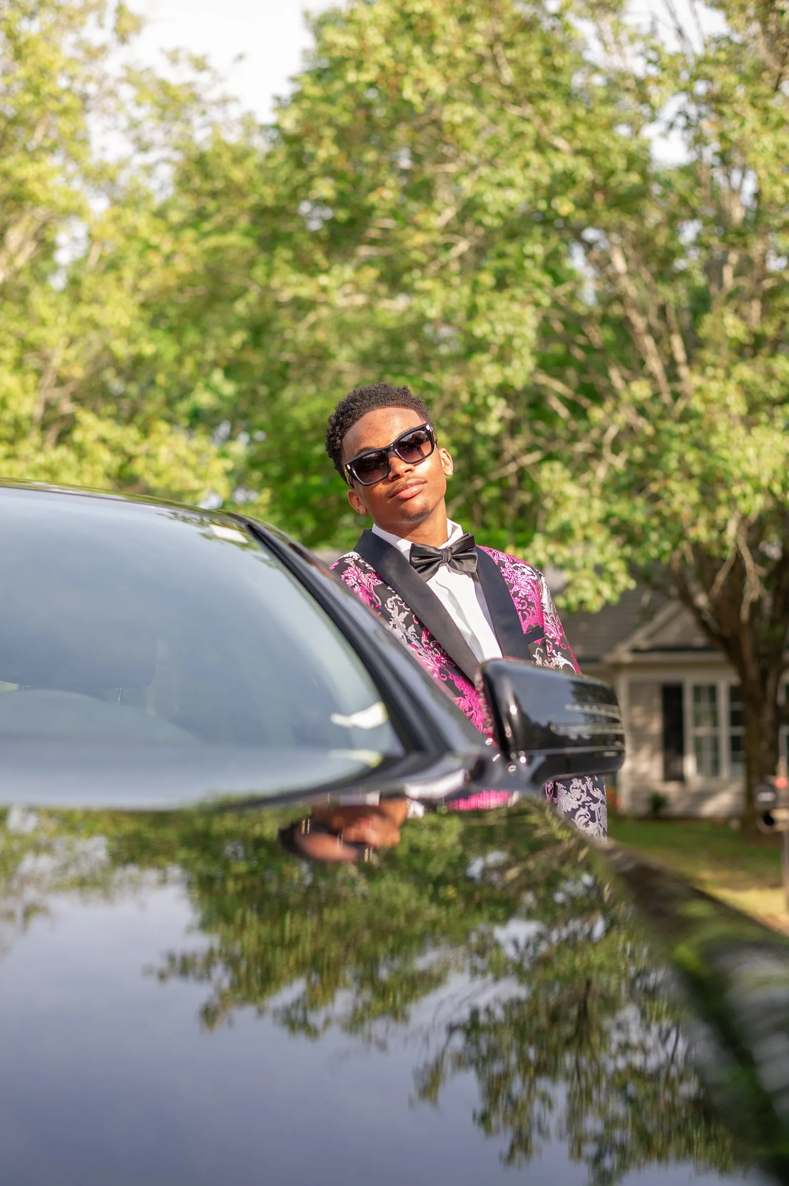 He leans on a black car, his reflection doubled in the hood