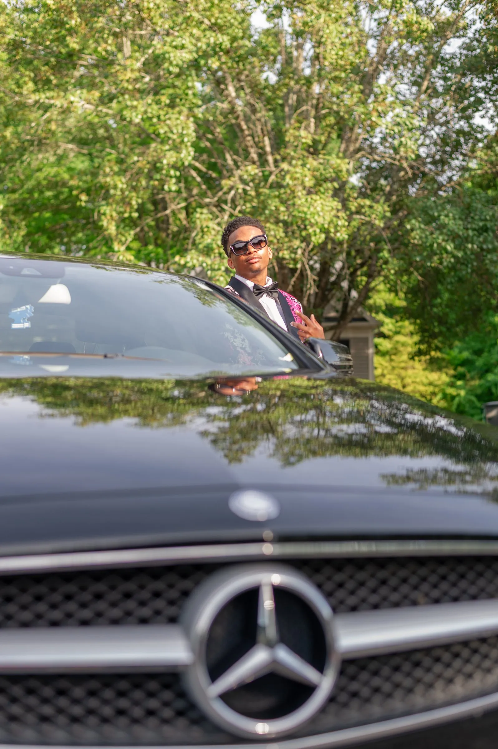 The Mercedes star in the foreground and him in sunglasses leaning on the car
