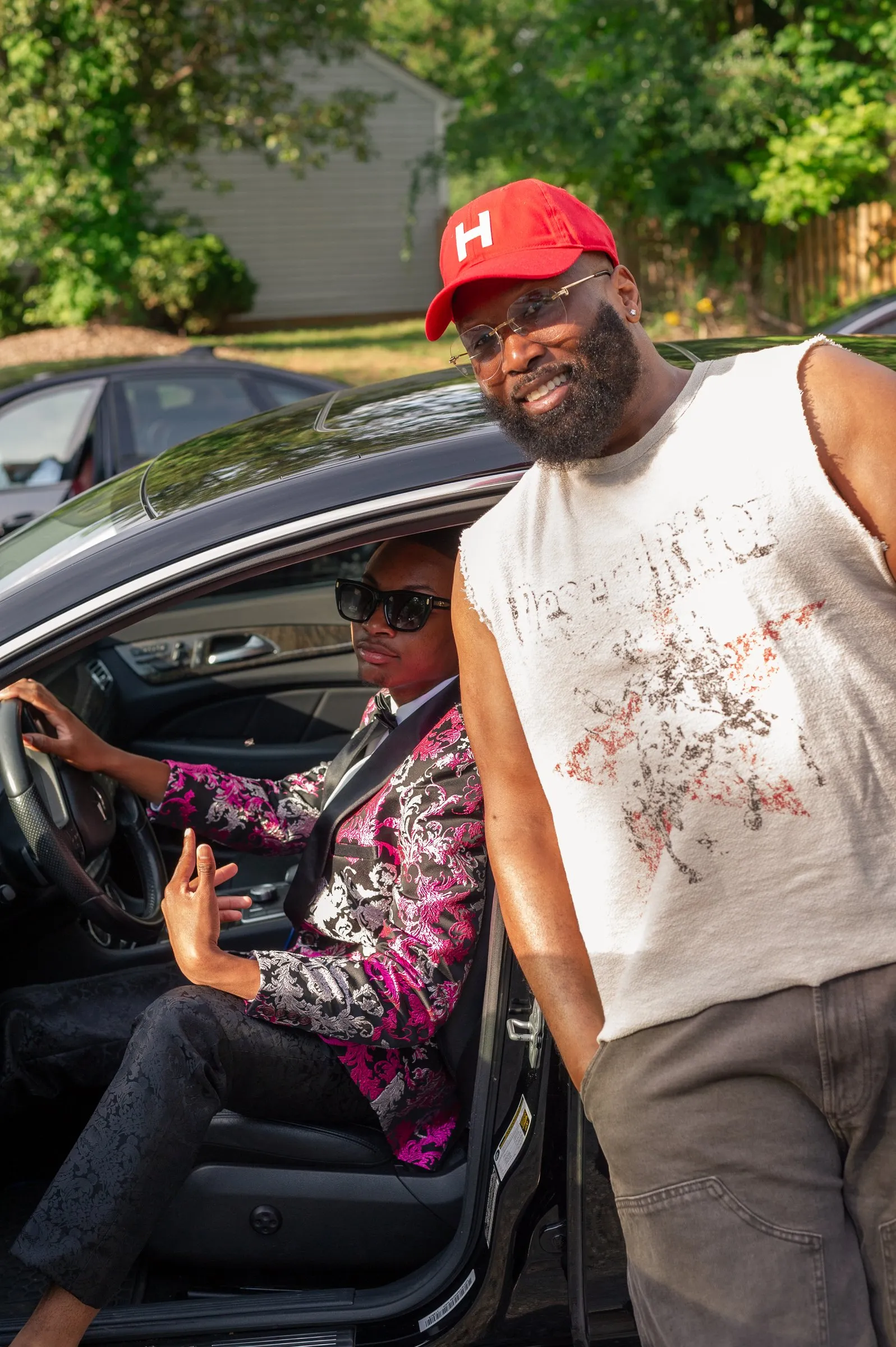 Behind the wheel of the Mercedes, he flashes a peace sign beside a man in a red cap