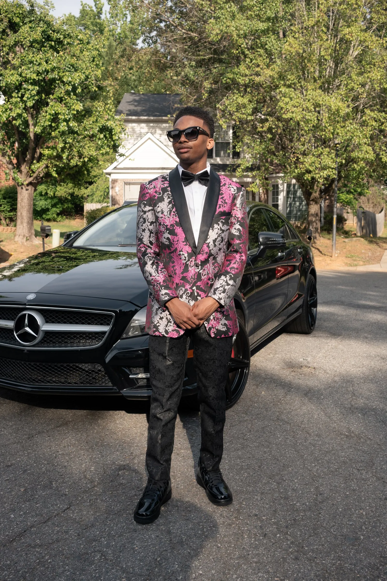 He stands in front of the Mercedes in his pink floral jacket