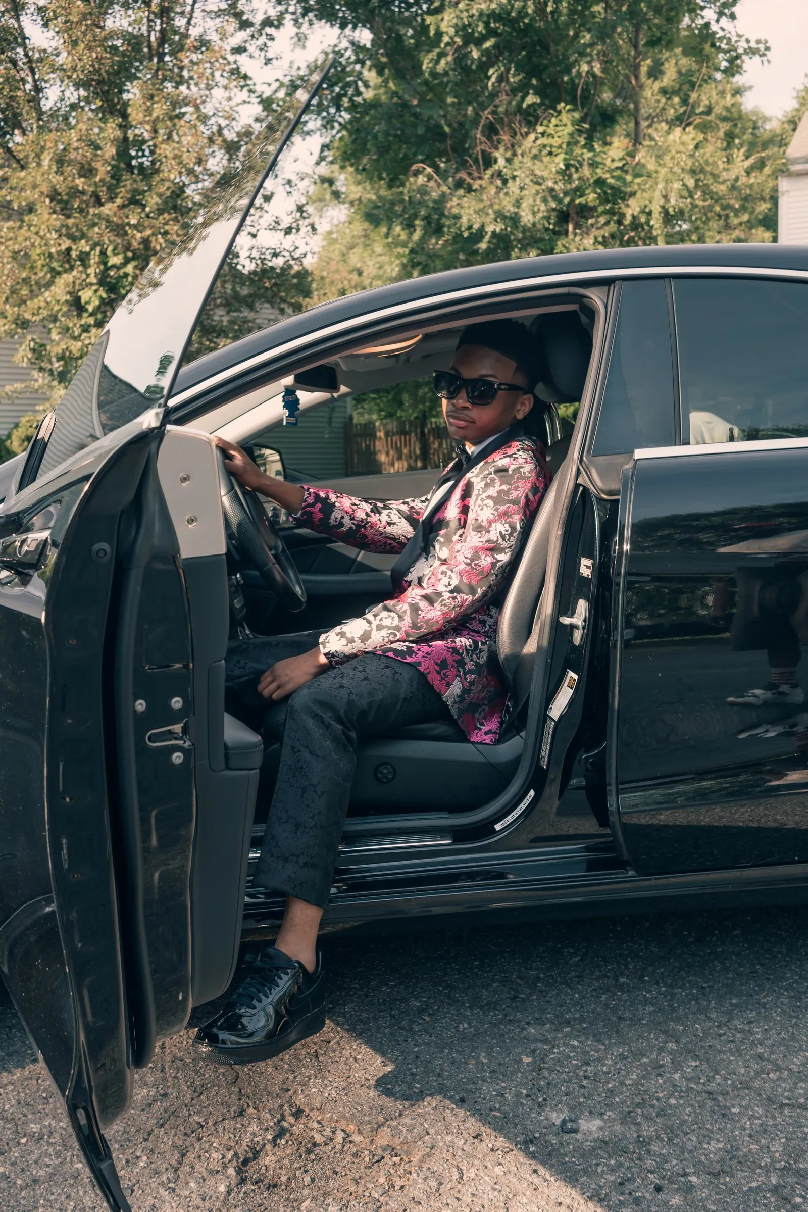 He sits in the driver's seat of the Mercedes with the door open