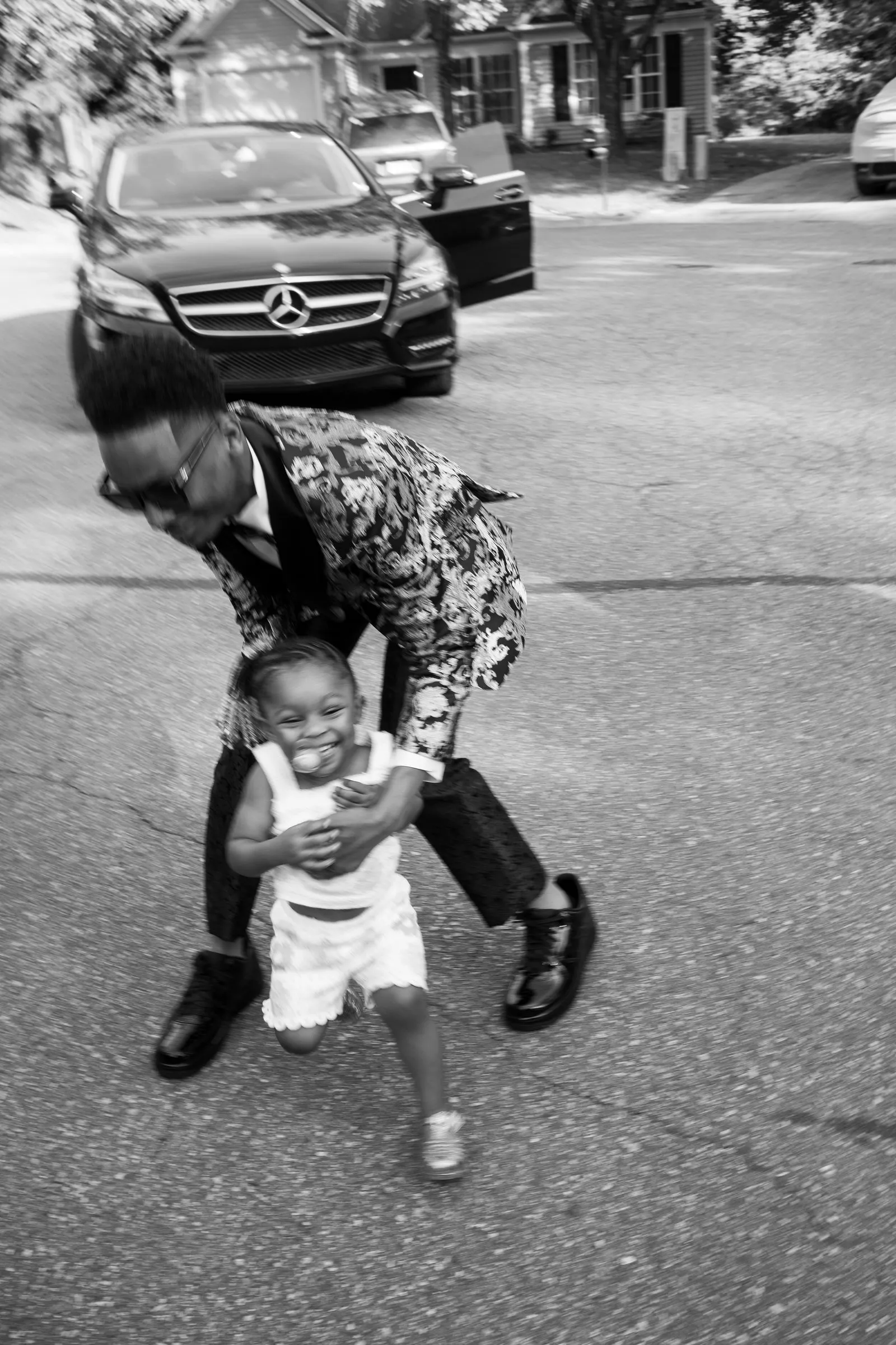Black and white photograph of him holding a toddler's hands as she walks