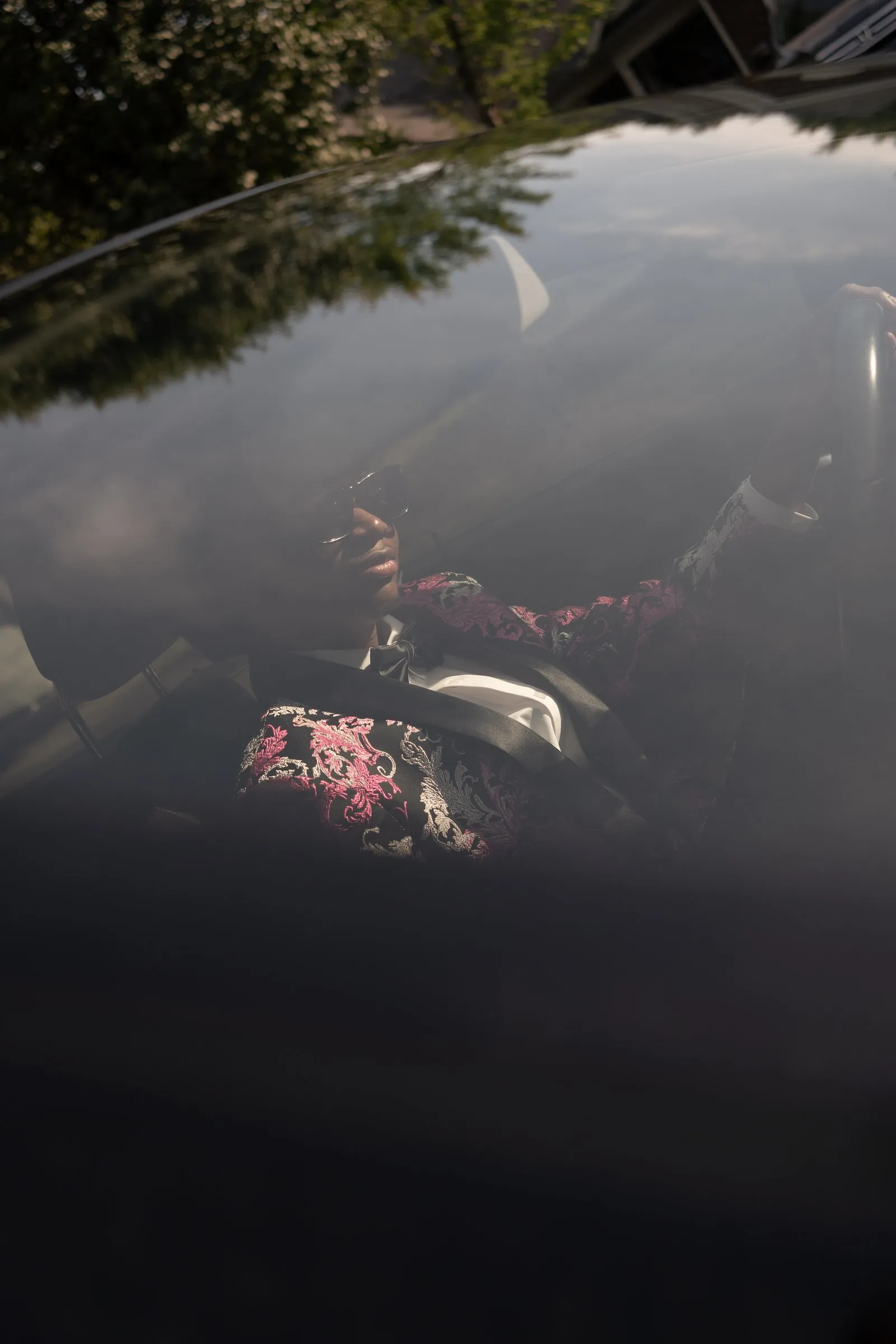 The reflection of his floral jacket in the dark car glass