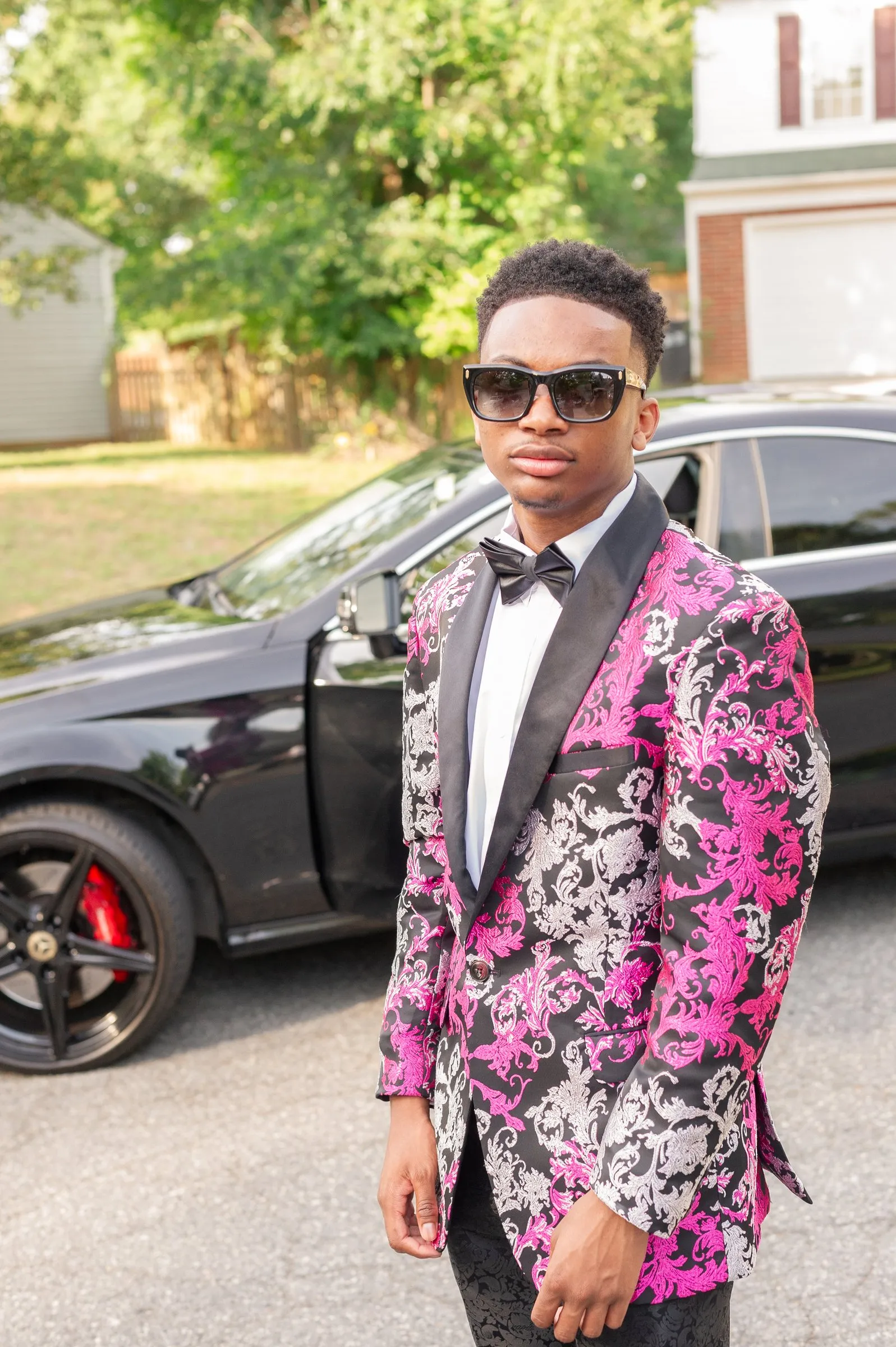 Prom portrait in the street, hands at his sides, a black car parked behind him