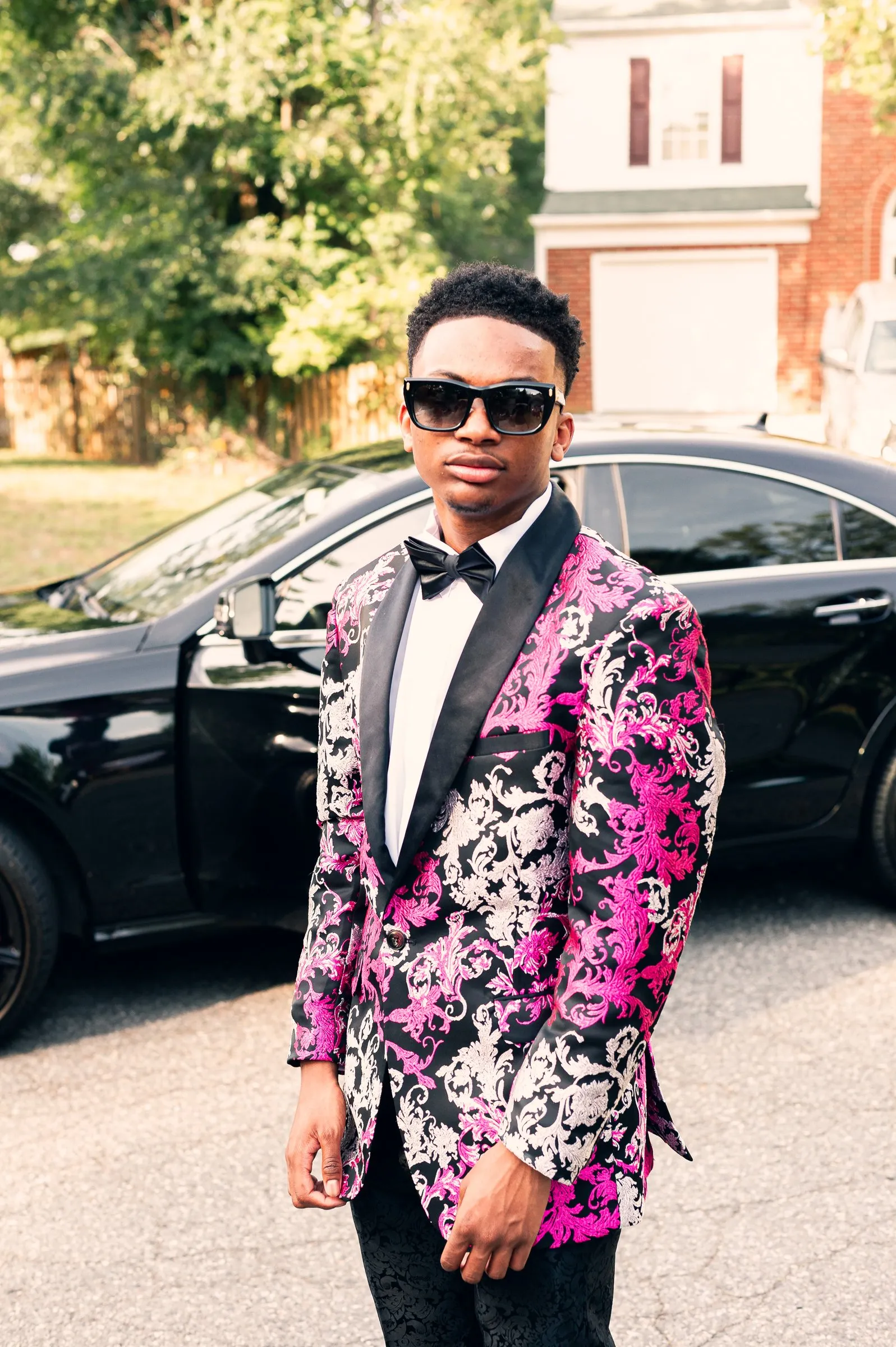 Portrait in sunglasses with a brick house and a black car behind him