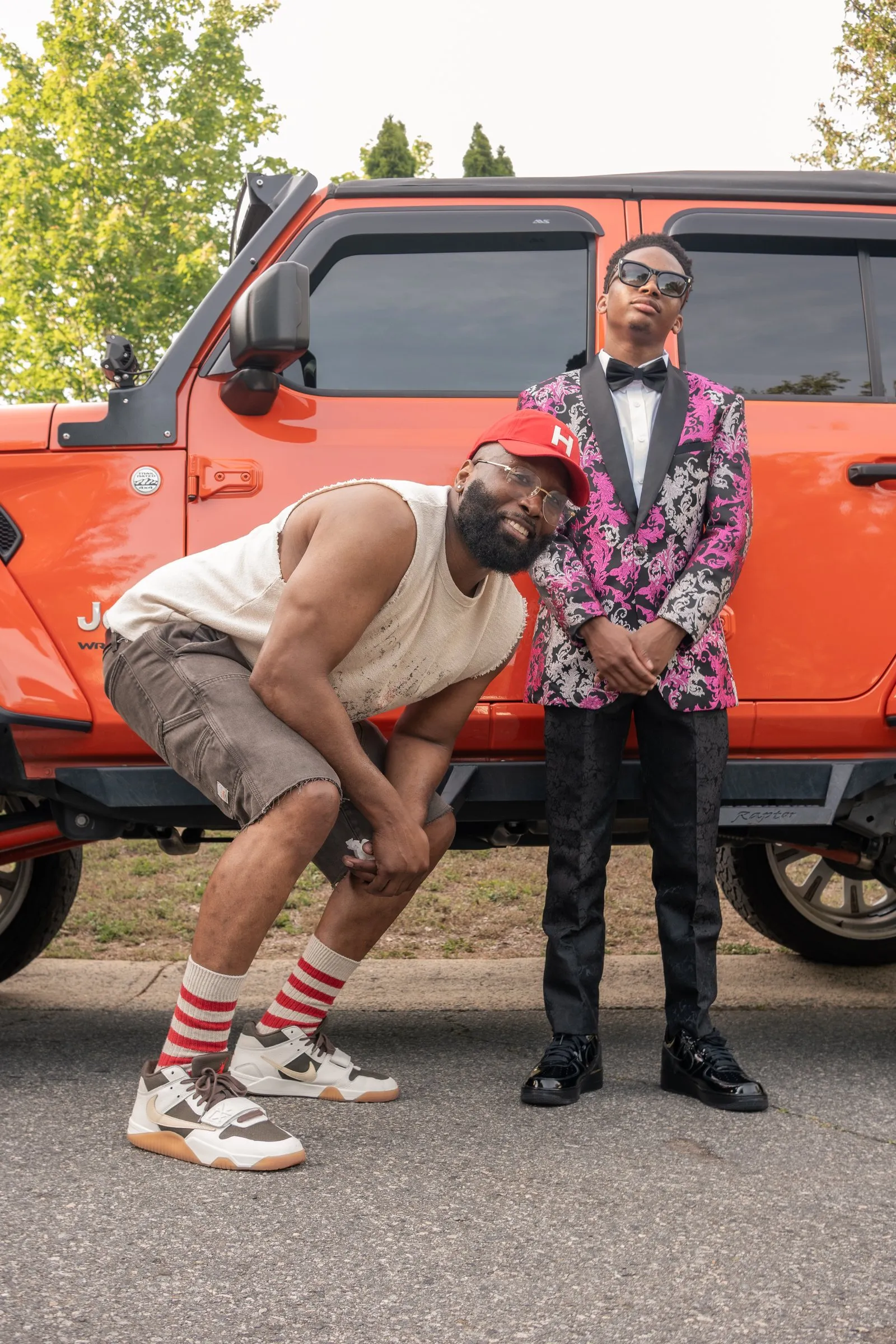He stands tall as a man in a red cap crouches beside him at the orange Jeep