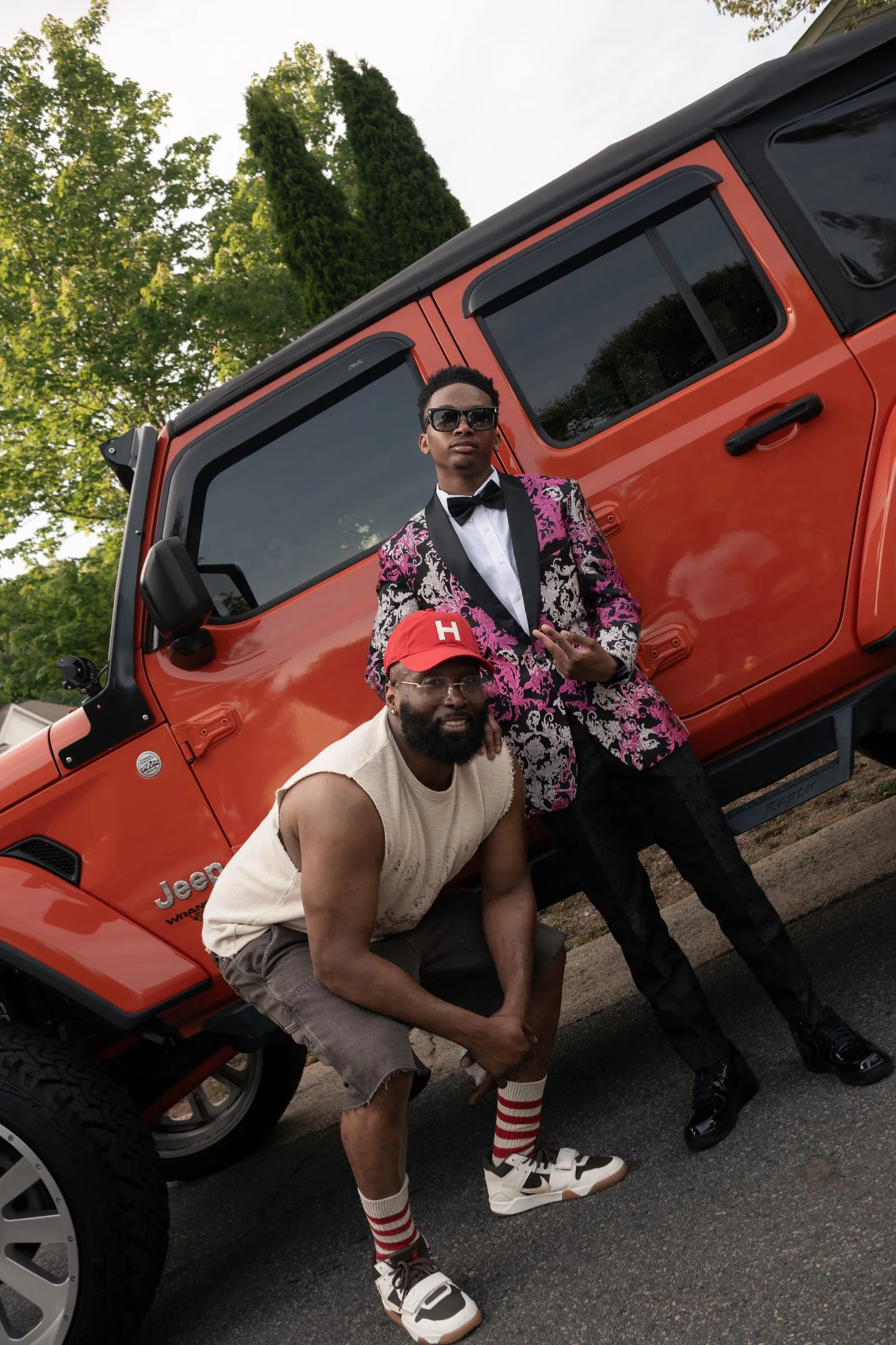 He leans on the orange Jeep above a man in a red cap