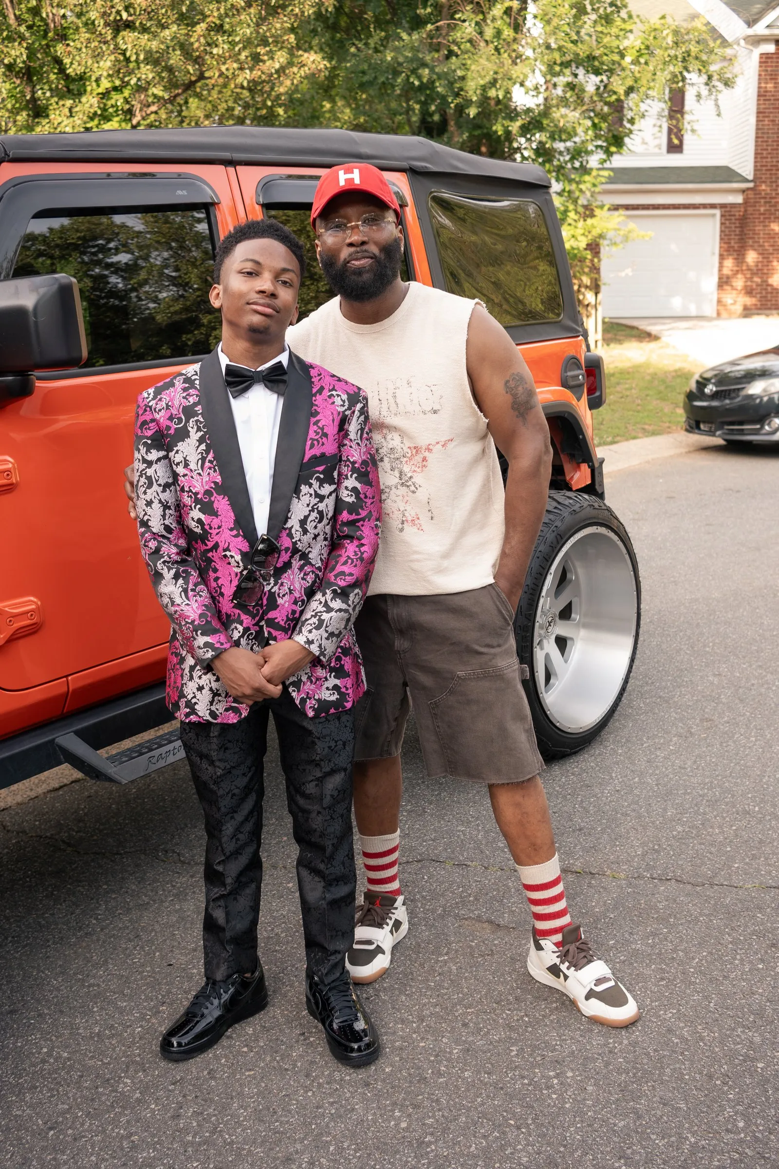 He stands with a man in a red cap in front of the orange Jeep