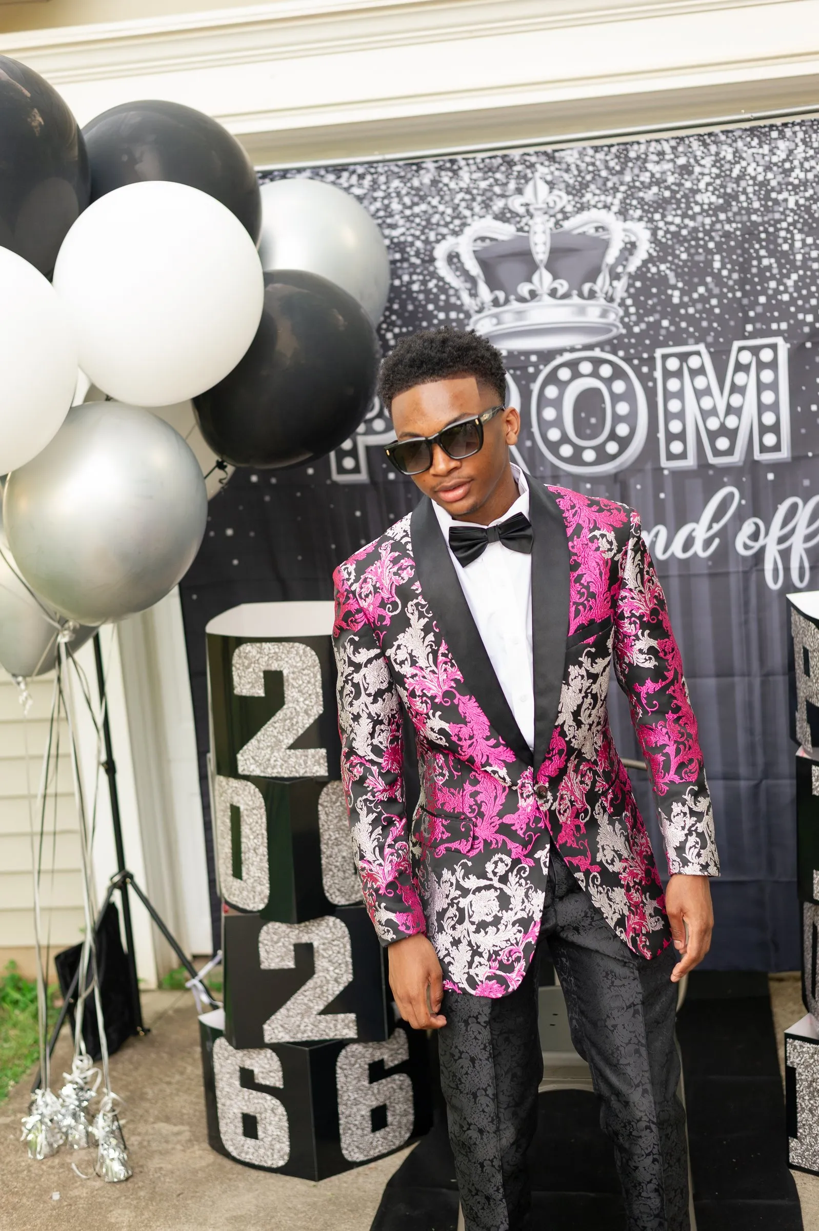 He stands with his hands at his sides in front of the Prom Send Off backdrop and balloon garland
