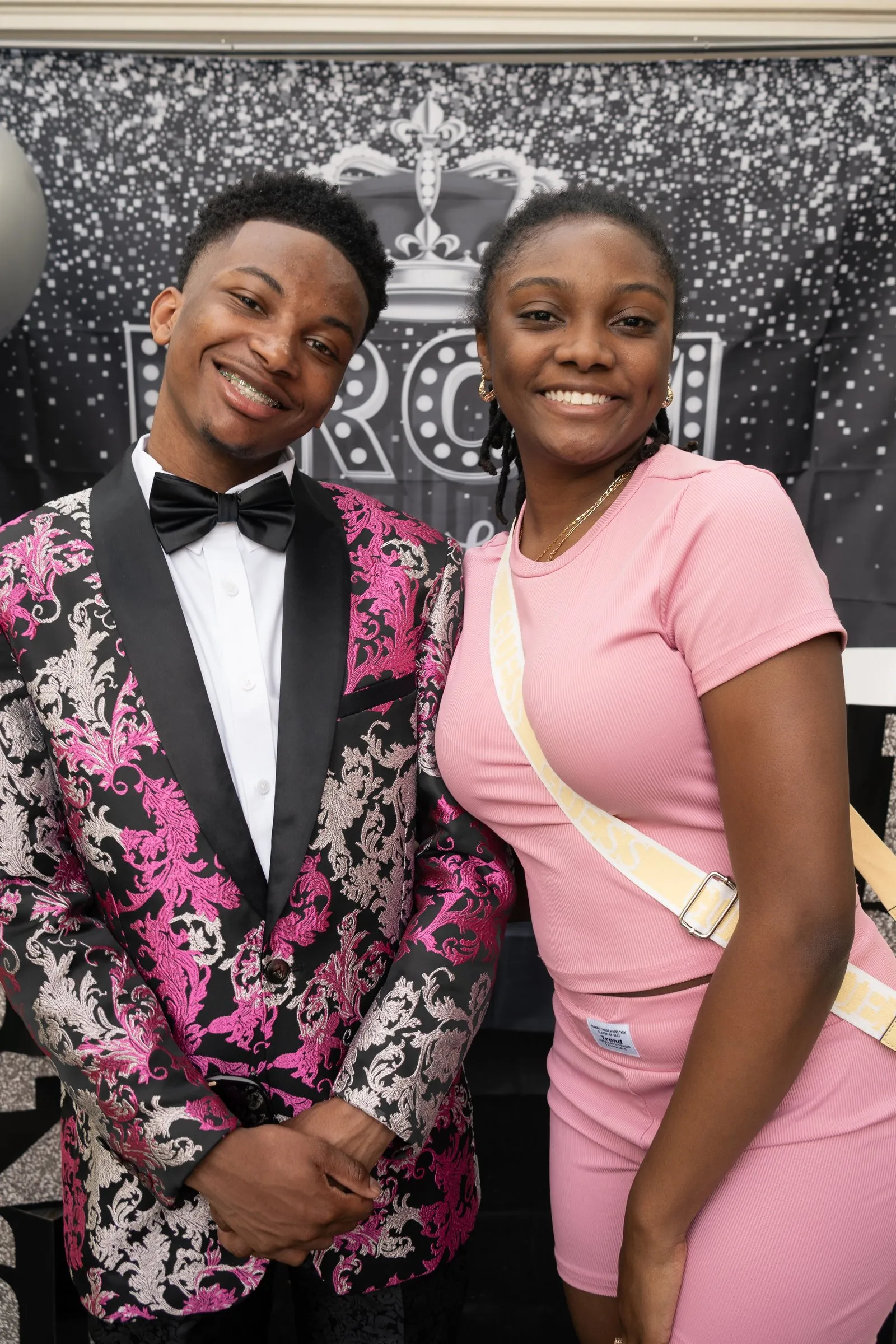 He smiles with a friend in pink in front of the Prom Send Off sign