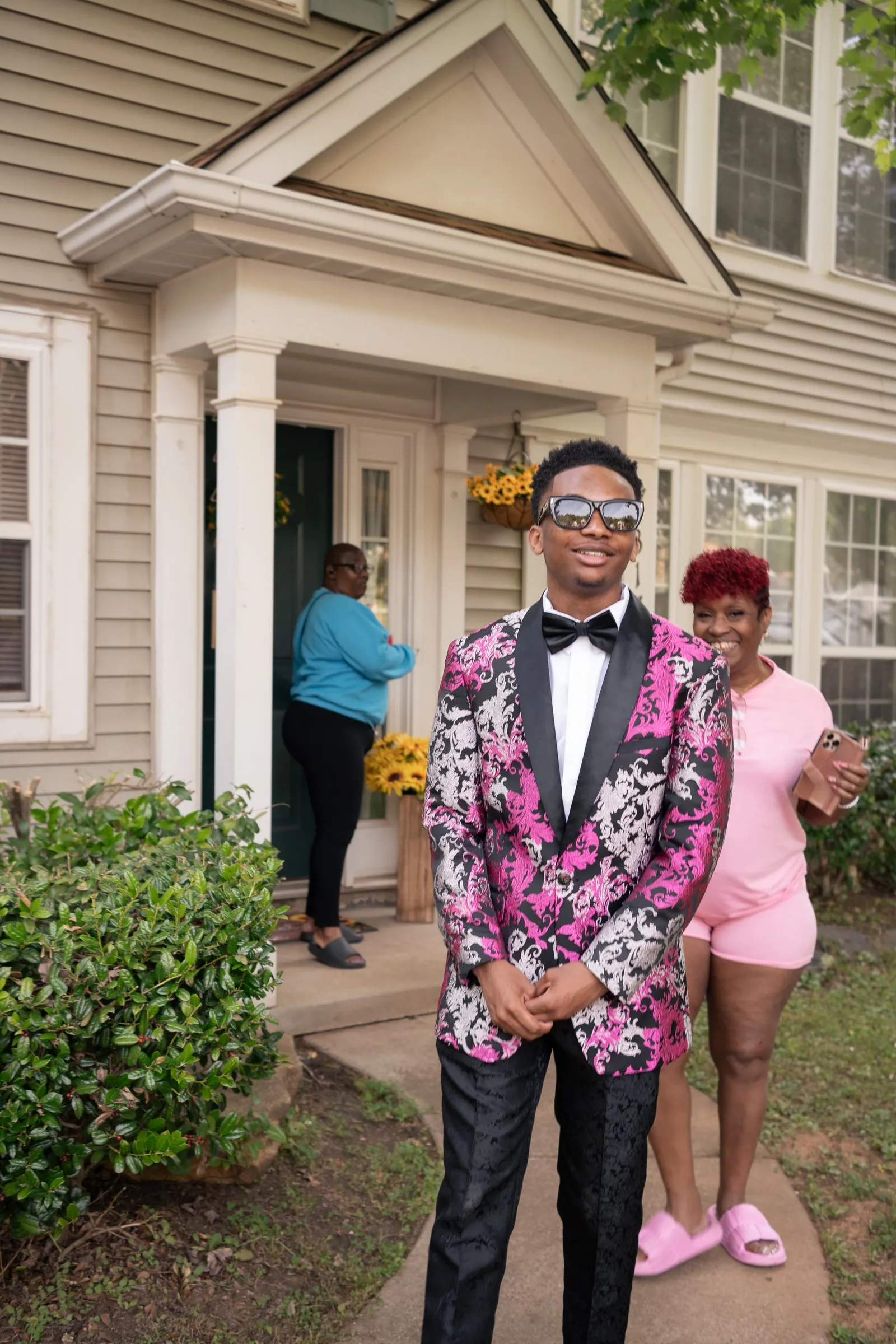 He stands at the front door in his tuxedo jacket beside a girl in pink