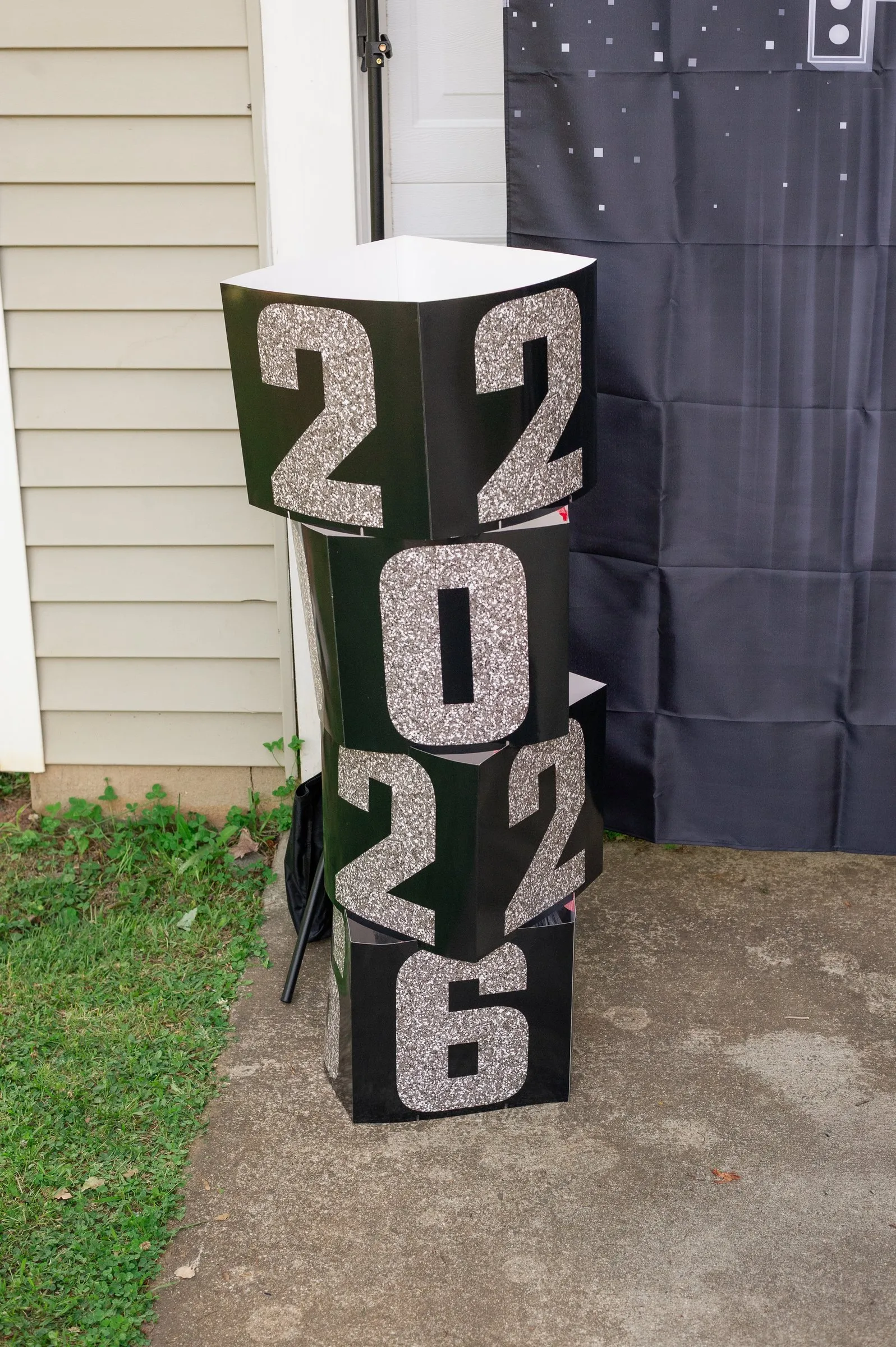 Black and silver glitter 2026 letter blocks stacked beside the prom send-off backdrop in the driveway