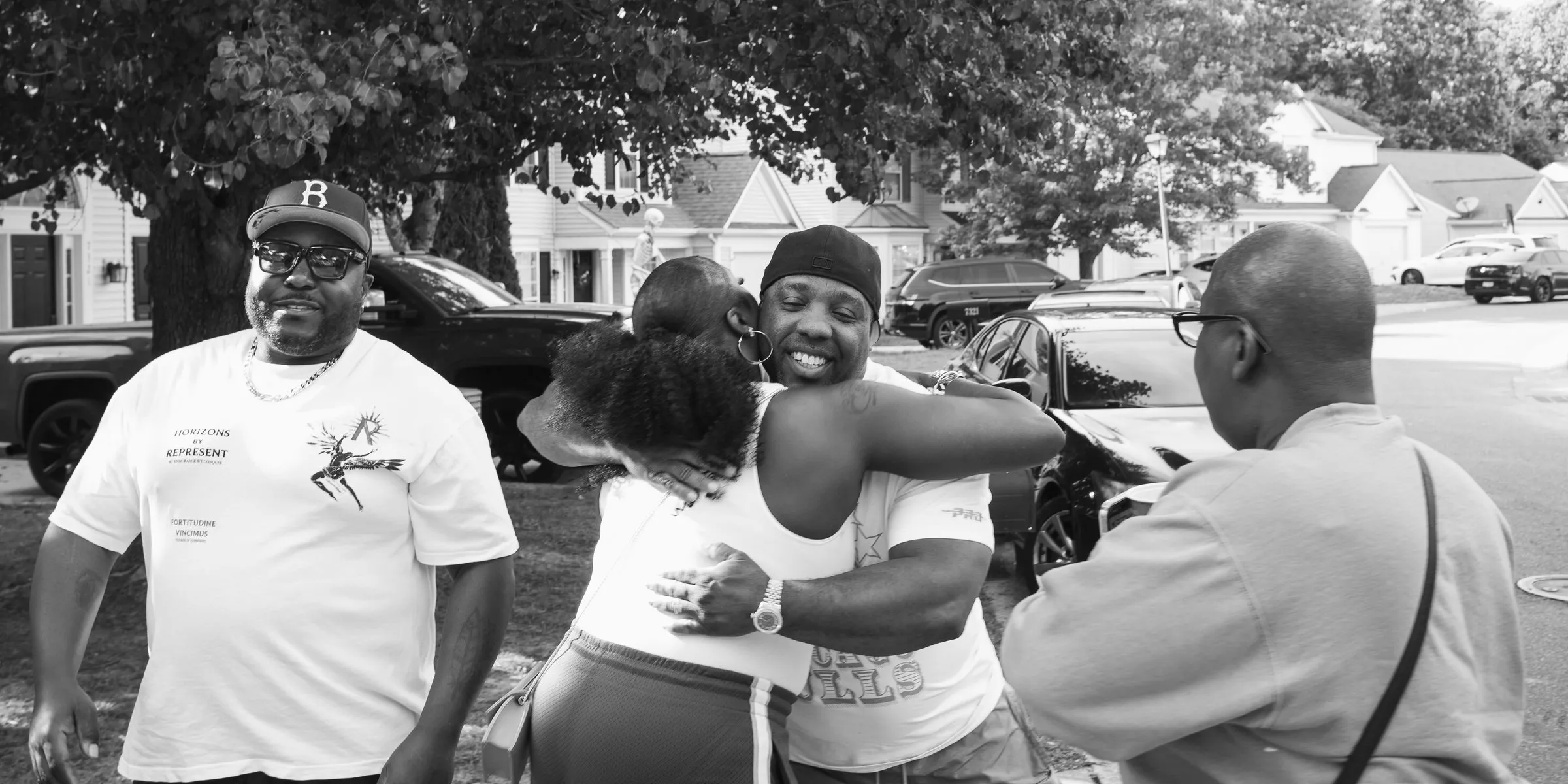 Black and white photograph of guests greeting each other with hugs in the street