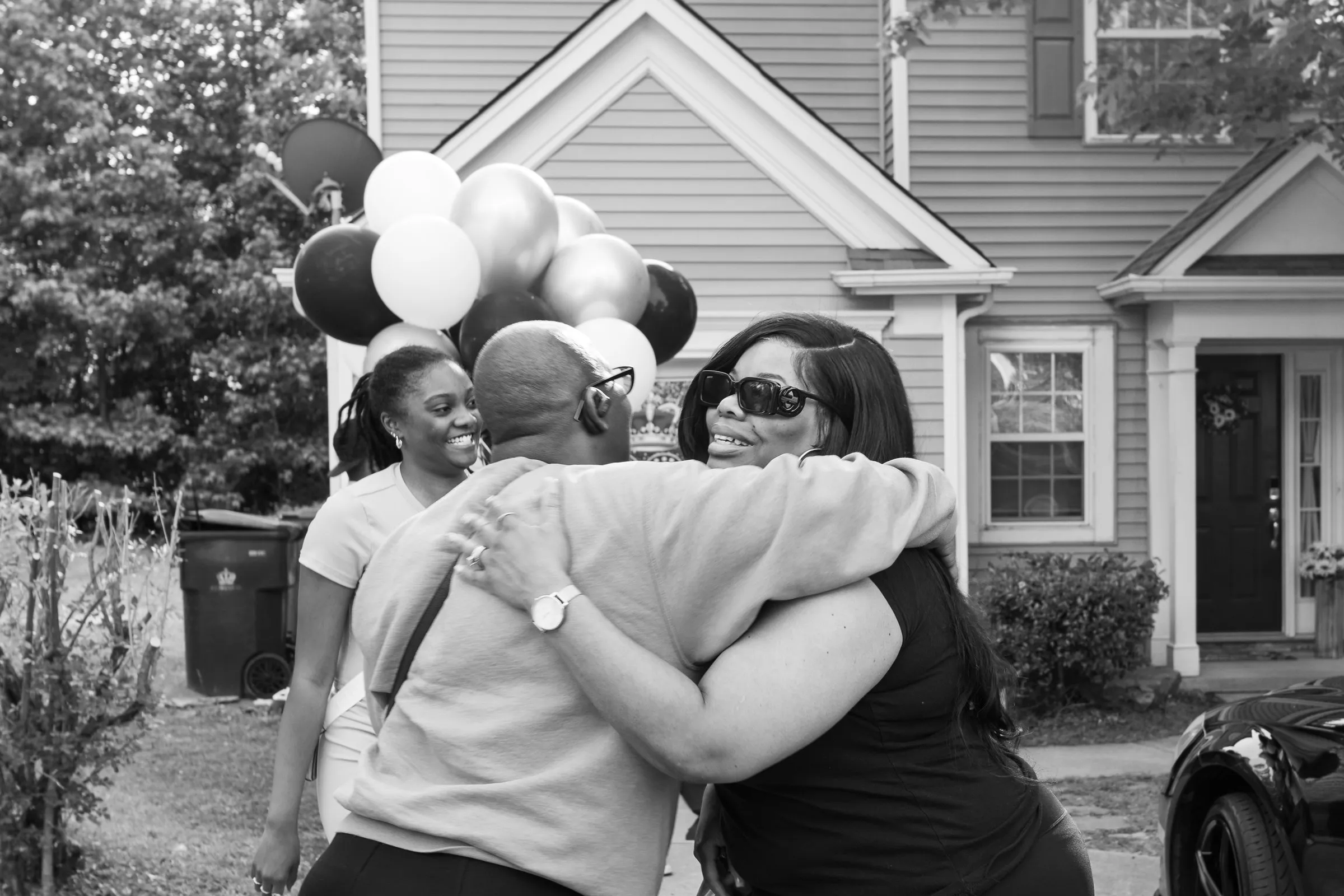 Black and white photograph of two women hugging in front of the house and balloons